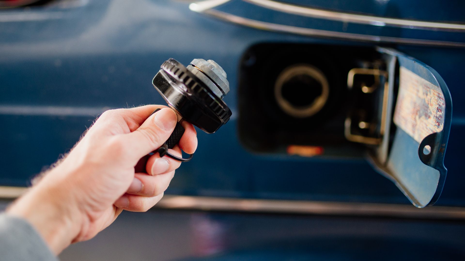 Car owner prepares to refuel at a gas station during the day while holding a fuel cap