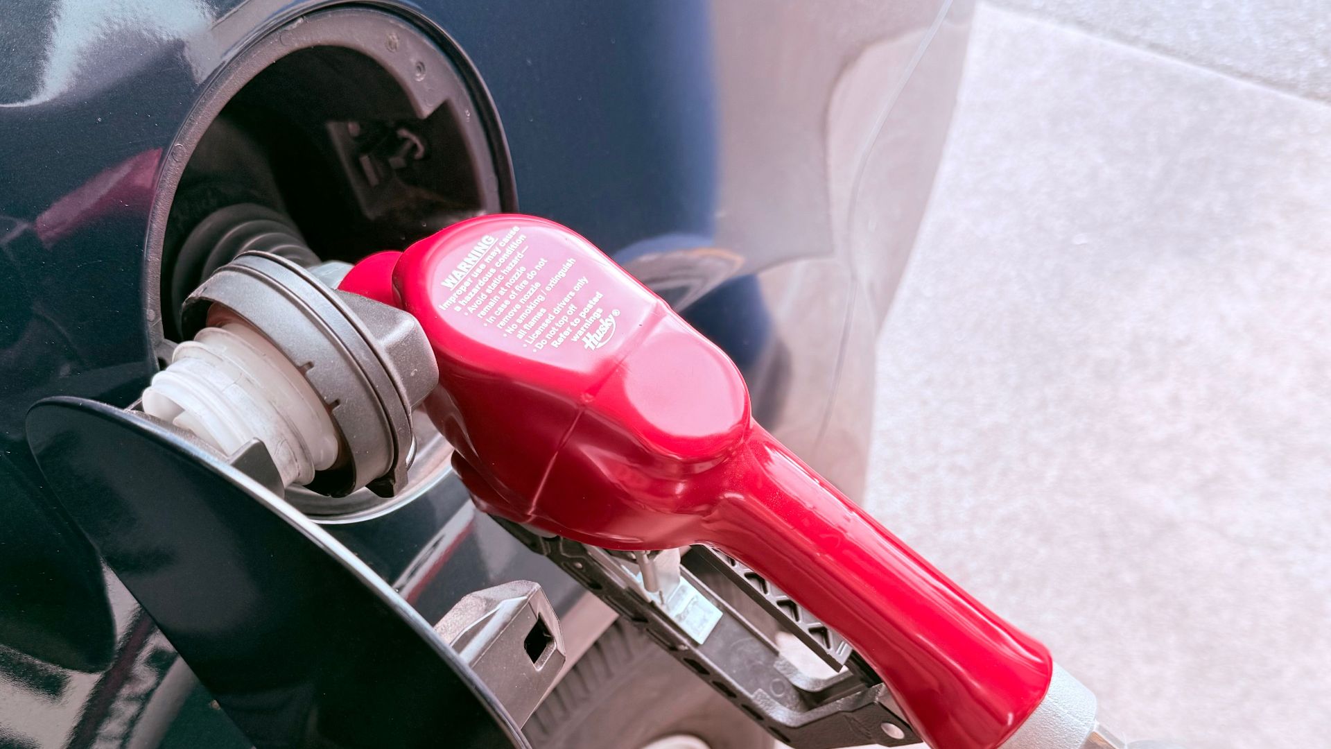 Close-up of a red gas pump fueling a car at a gas station, depicting the refueling process.