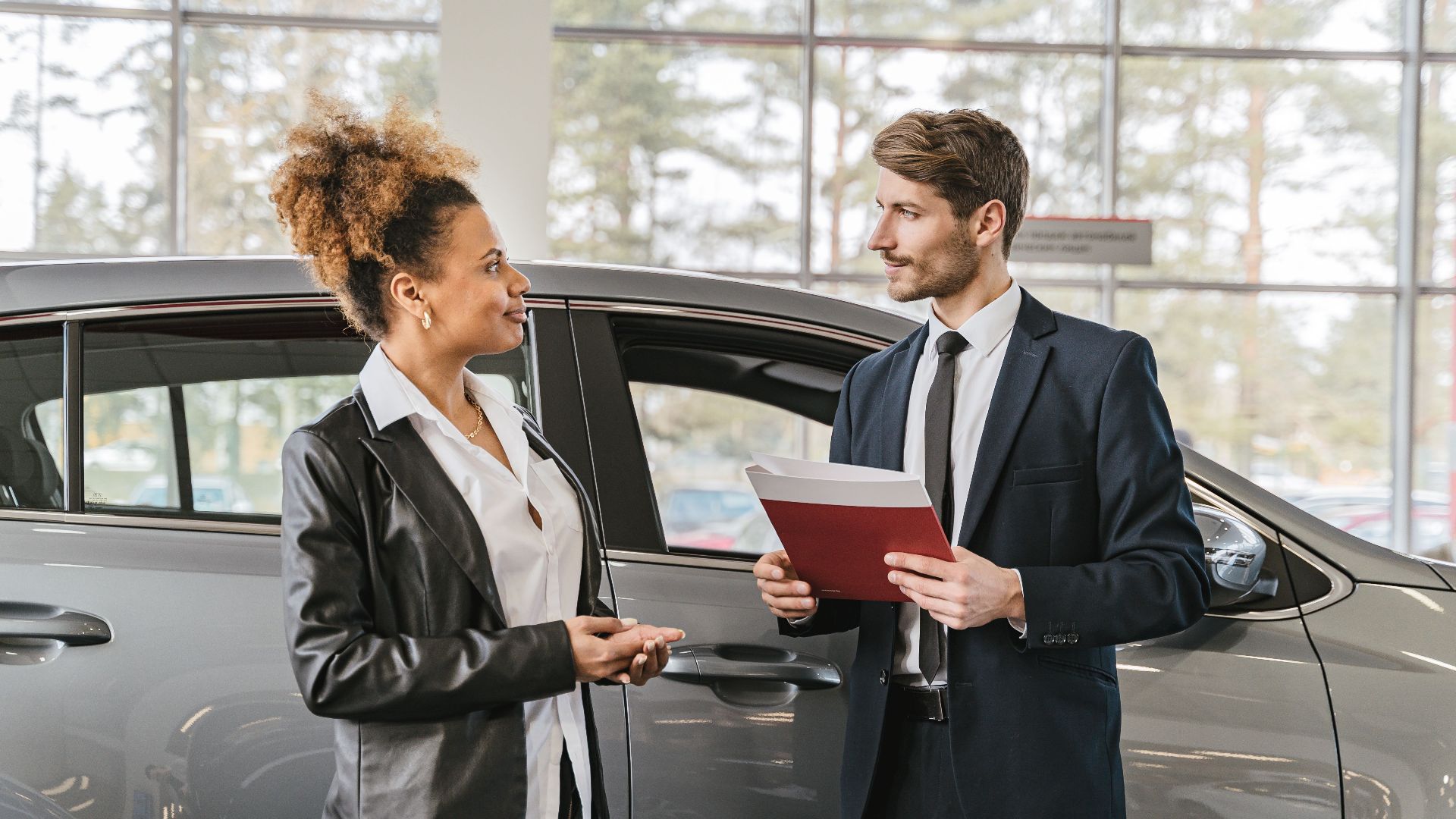 A woman discussing car purchase with a dealer inside a car dealership showroom.