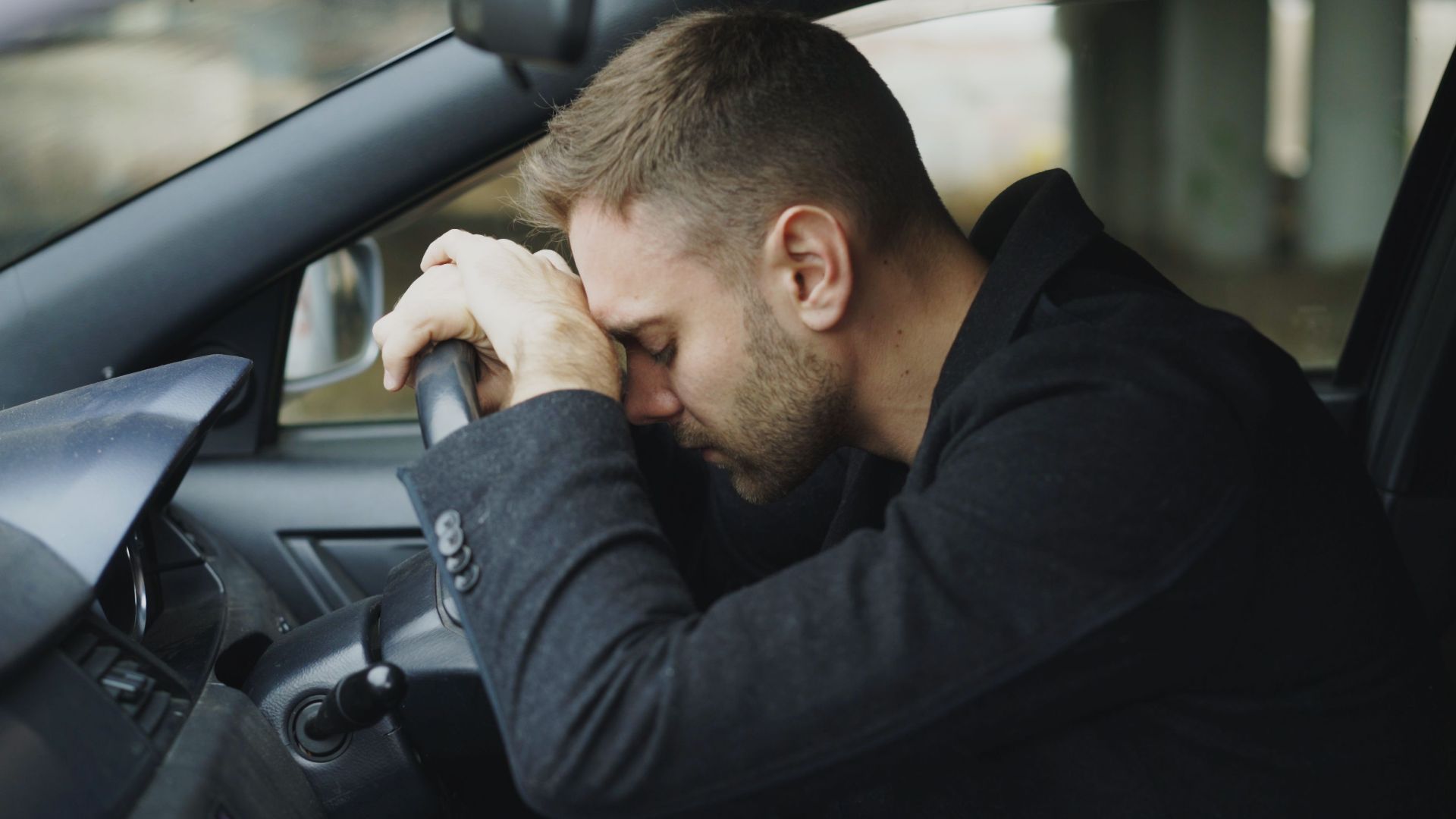 A man showing stress while sitting in a car, head on steering wheel.