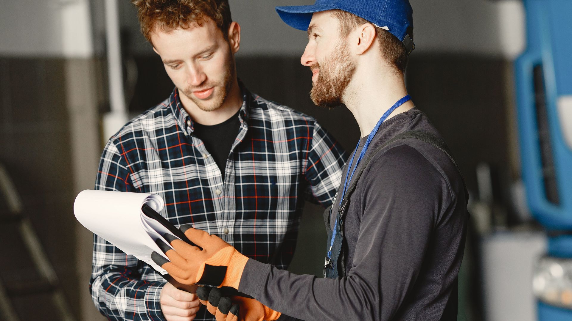 Mechanic in uniform consults with customer in garage setting beside a blue truck.