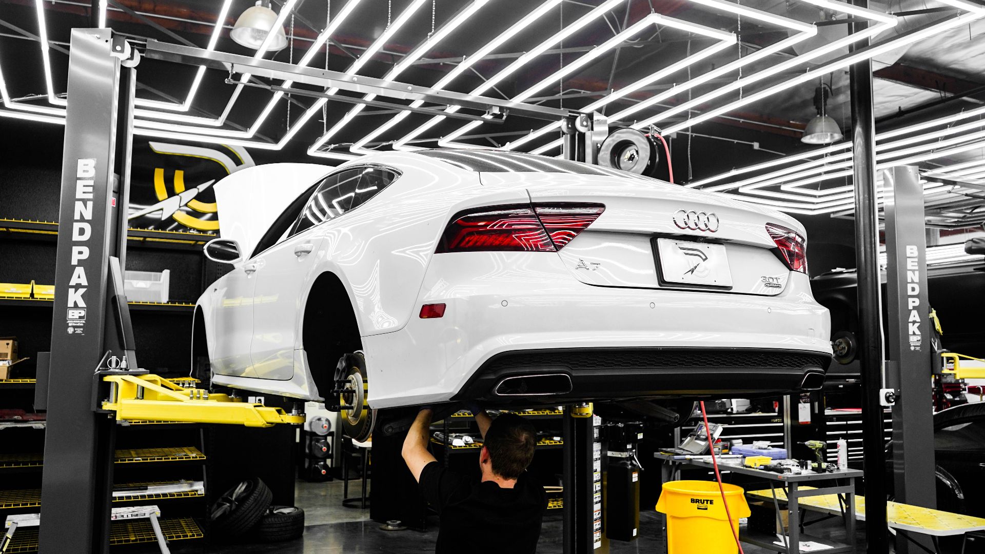 White luxury car being serviced by mechanic in a modern garage setting.