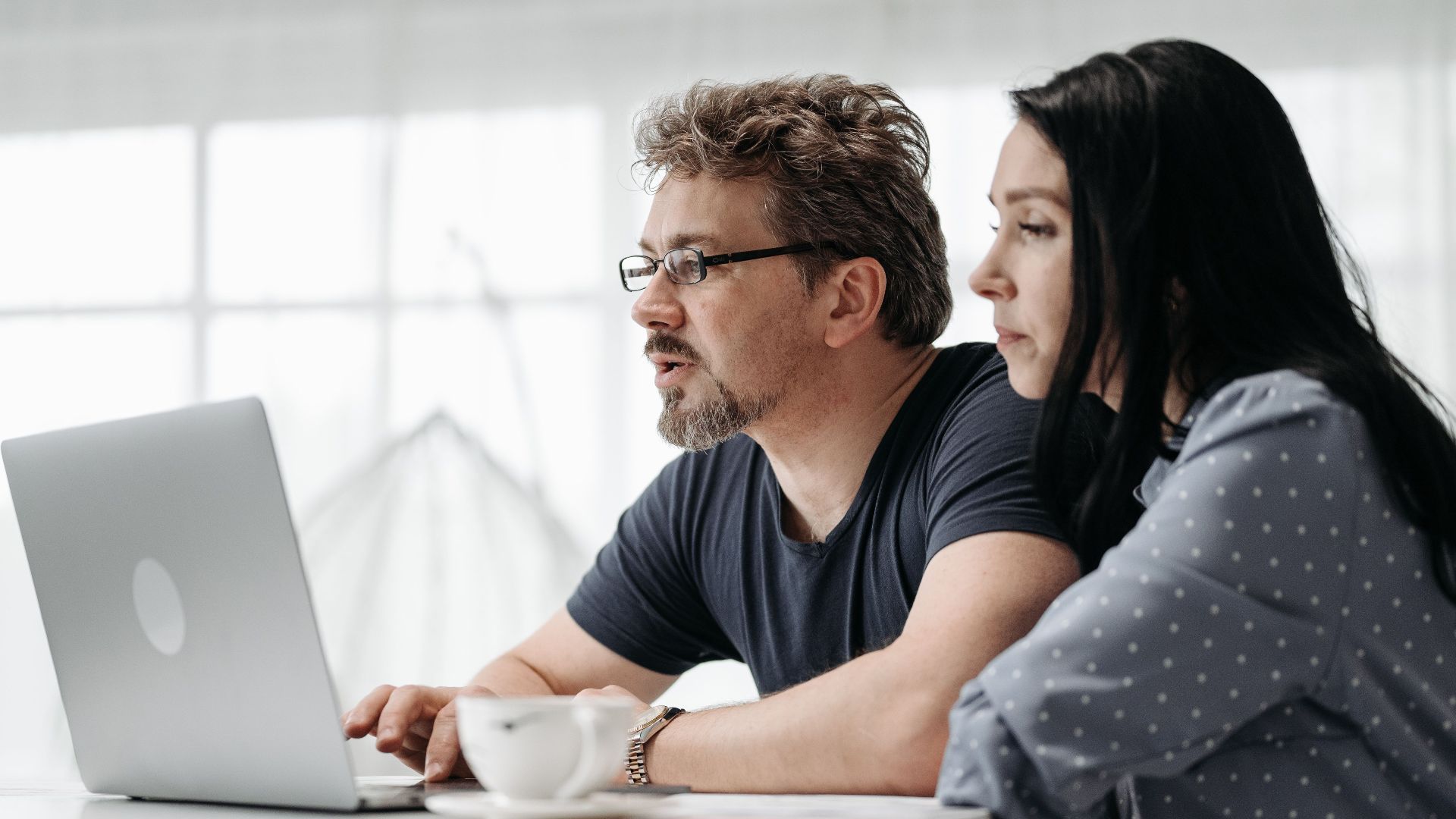 A couple uses a laptop at home in a bright and cozy setting, collaborating closely.