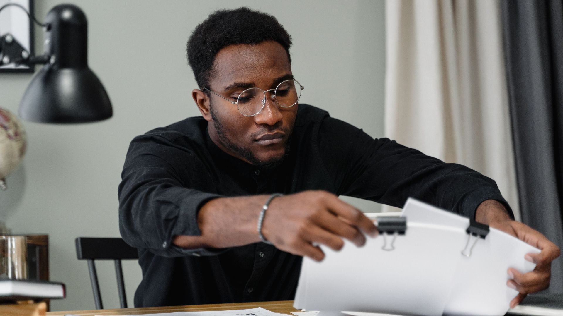 Professional man with glasses reviews documents at a desk in an office setting, emphasizing concentration.