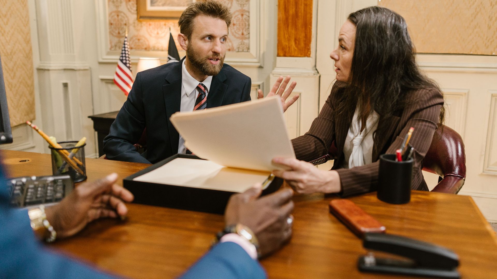 Diverse group in a corporate office engaged in a formal meeting. Professional attire and documents suggest a business discussion.