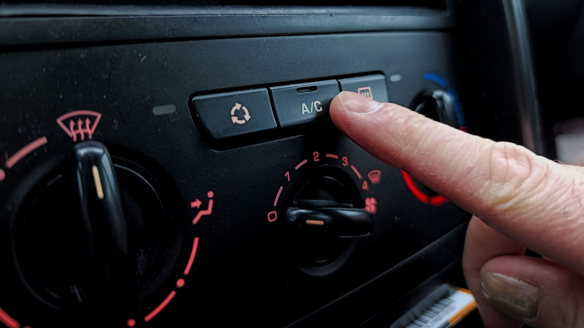 Close-up of a person adjusting a car's air conditioning system inside a vehicle cabin.