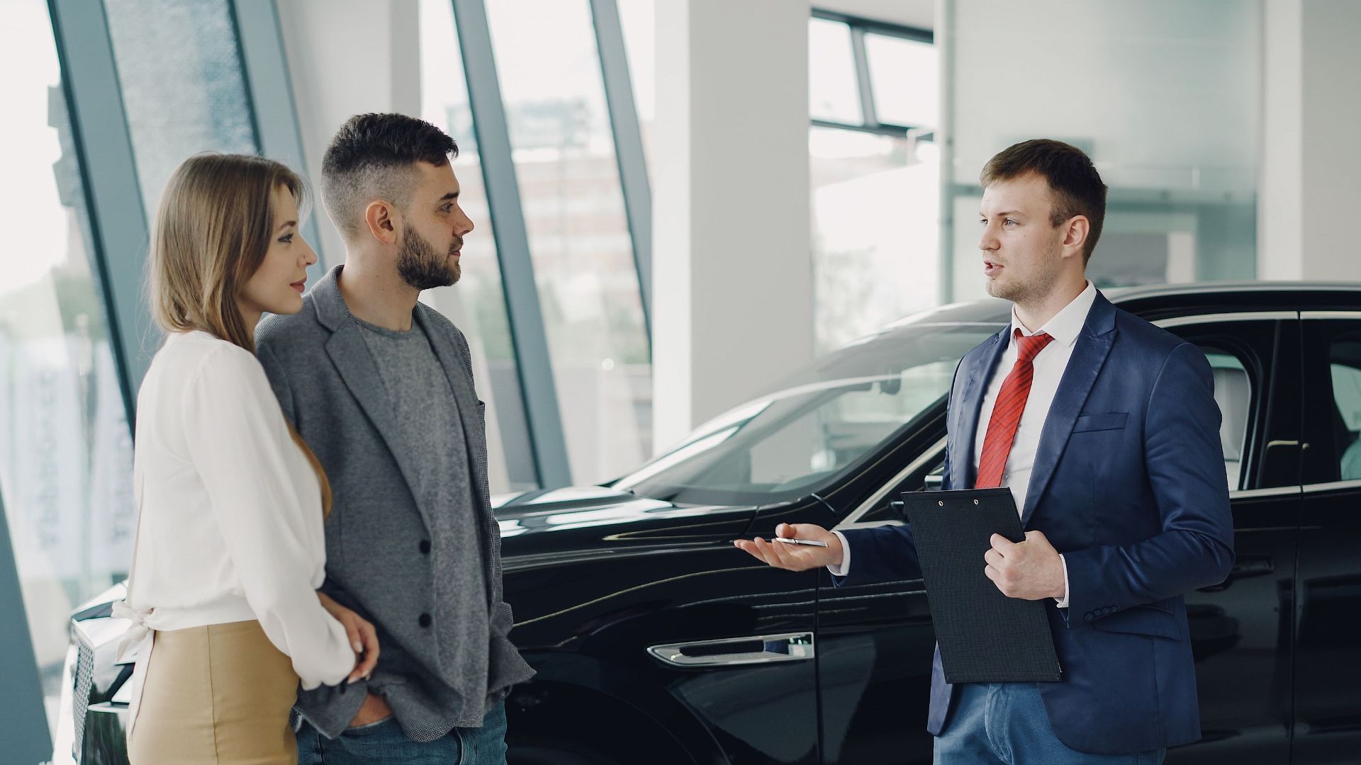 A couple talks with a salesman in a modern car showroom, considering a vehicle purchase.