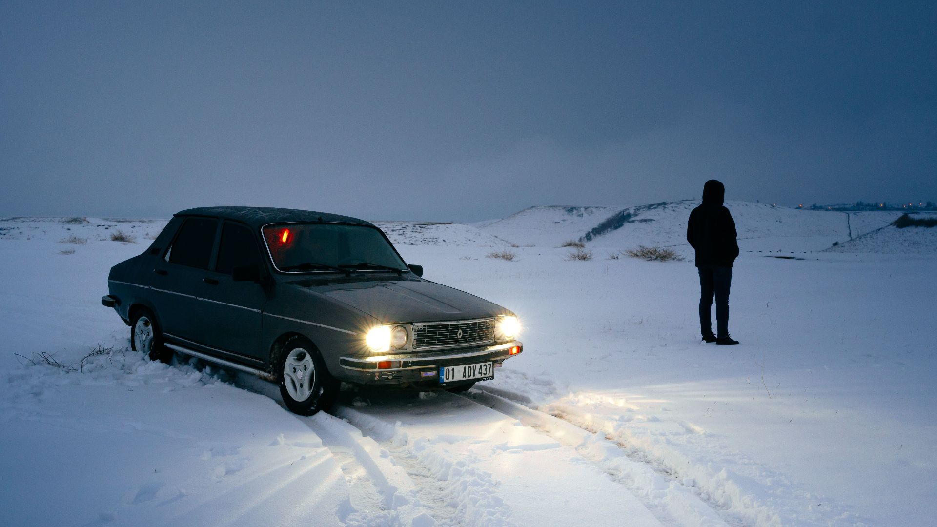 Vintage car and person on a snowy evening in Adıyaman, Türkiye.