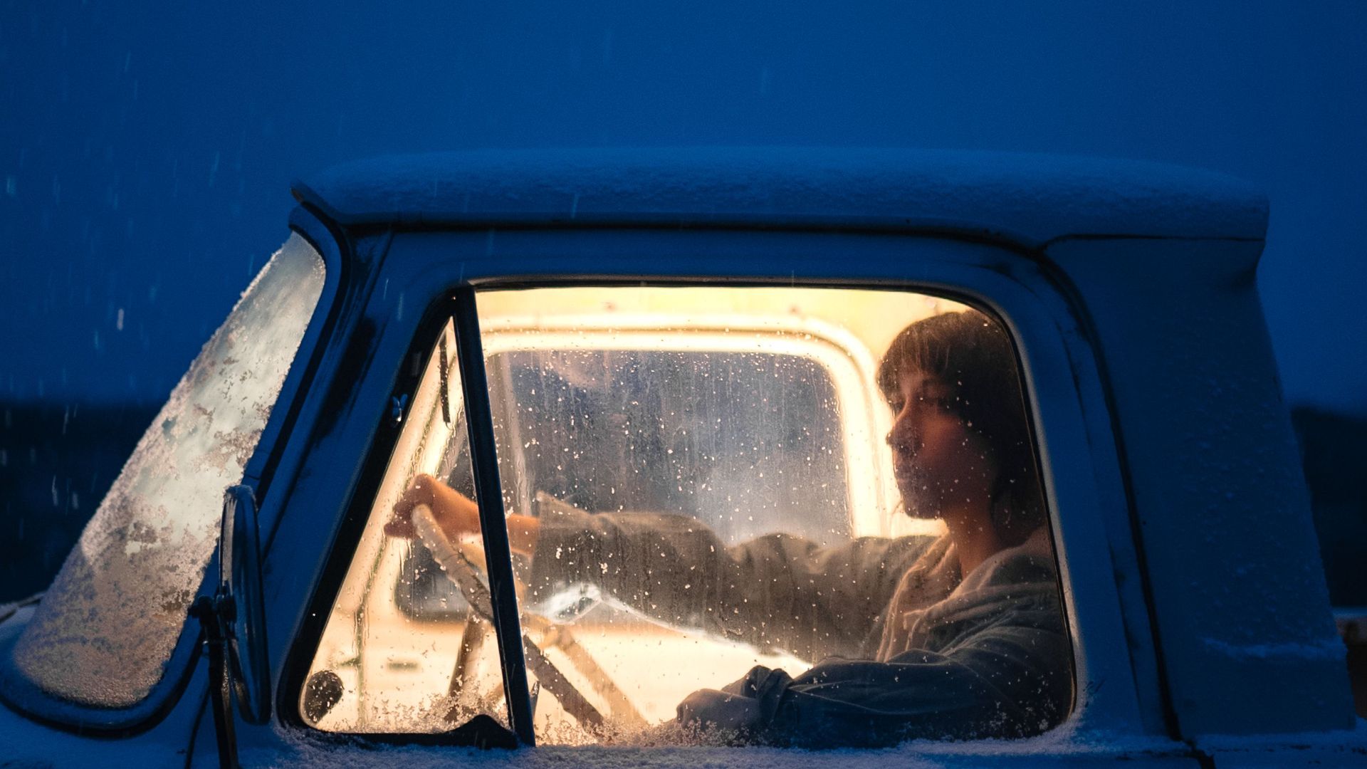 Person driving a vintage truck on a snowy night, illuminated from within, capturing a moody winter scene.