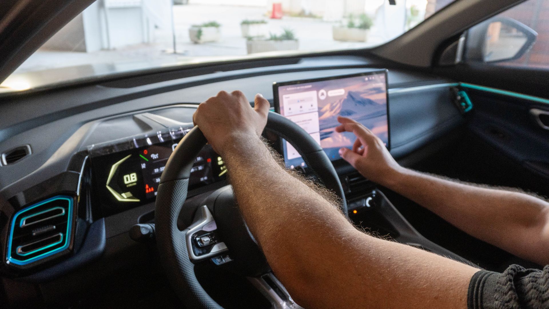 Man uses car touchscreen infotainment while driving in urban area. High-tech dashboard and modern interface.