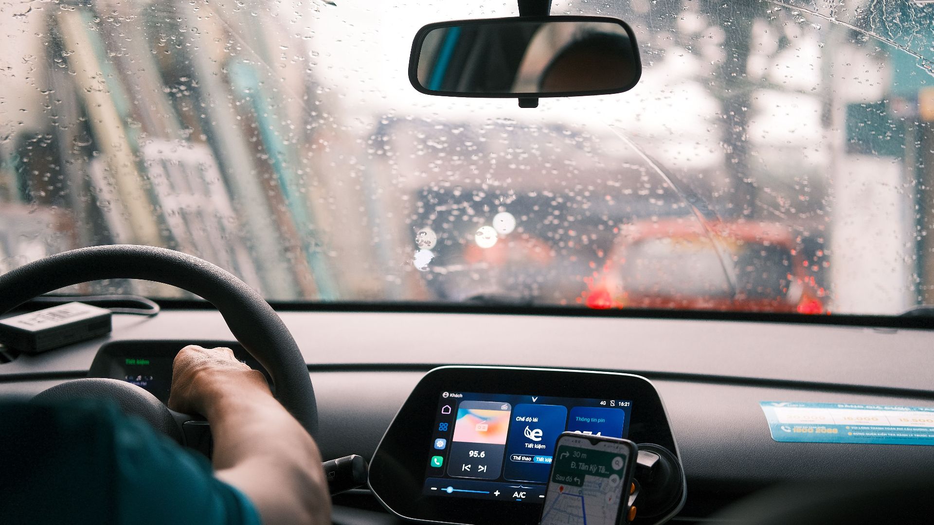 Interior view of a car during a rainy drive in city traffic, focus on dashboard and windshield.