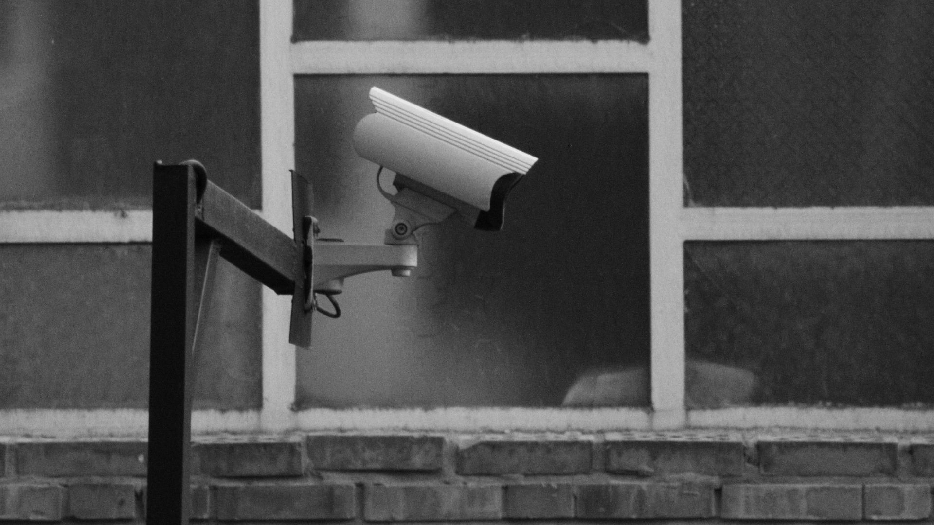 Monochrome image of a CCTV camera mounted on a building exterior.