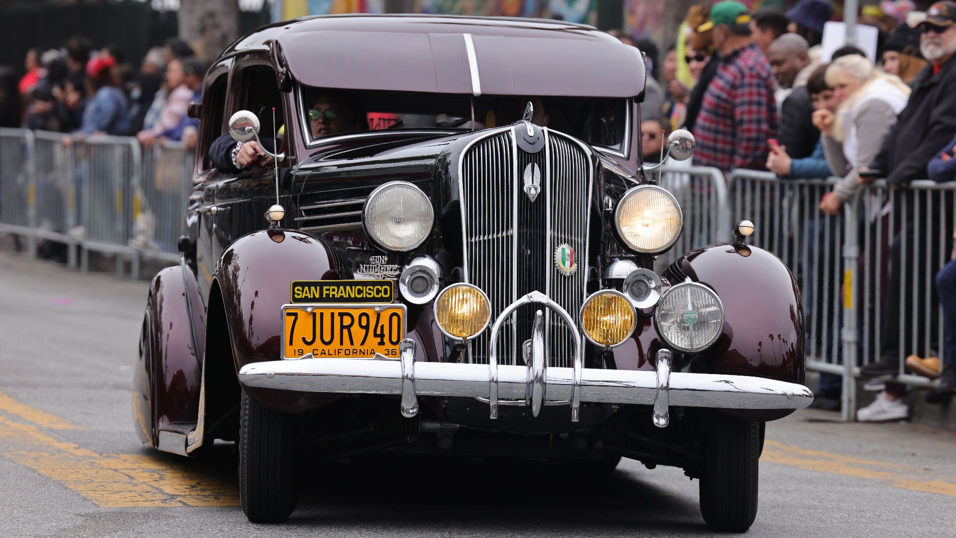 A classic vintage car drives through a street parade in San Francisco with spectators lining the street.