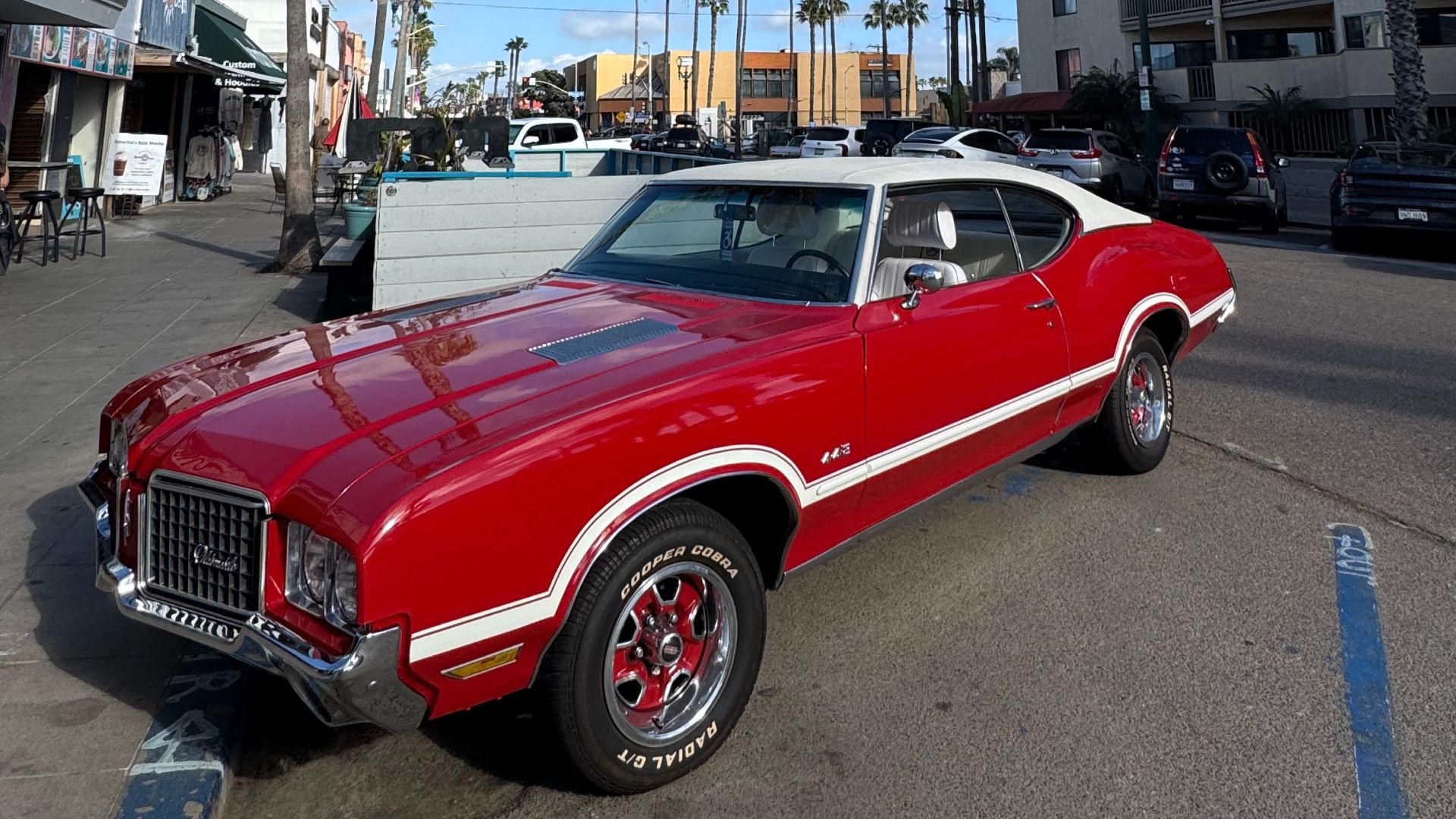 Vintage red muscle car parked under palm trees on a sunny day in San Diego.
