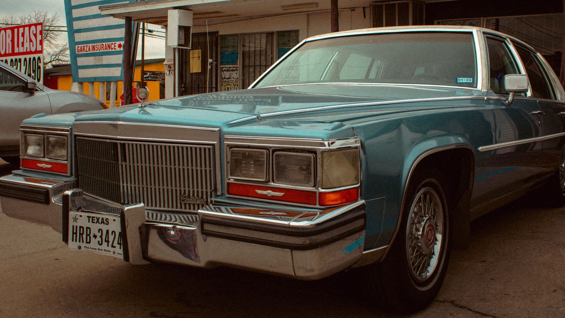 A vintage Cadillac parked outside a storefront under a cloudy sky, evoking nostalgia and classic urban charm.