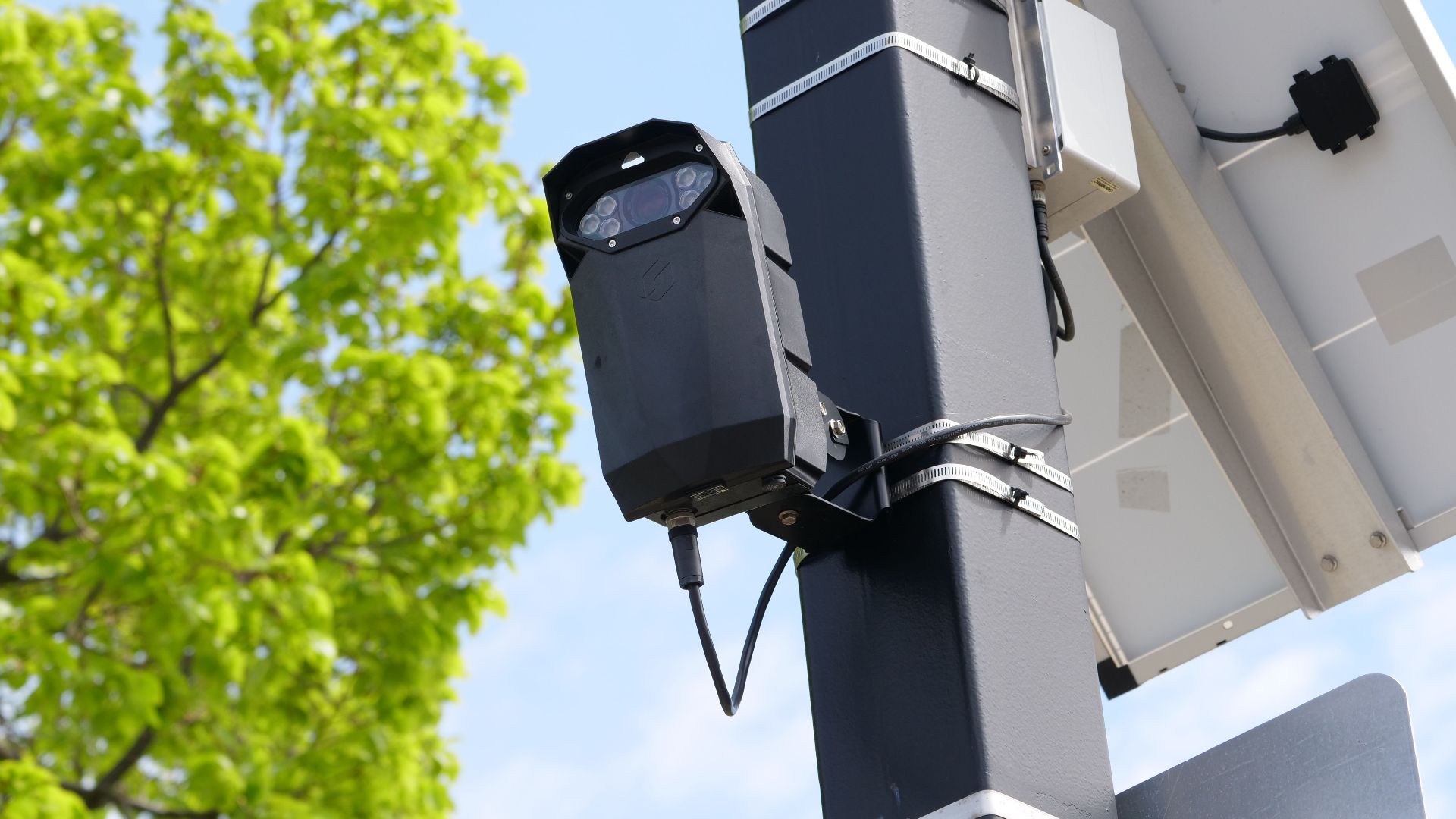 A modern surveillance camera powered by solar energy mounted on a street pole.