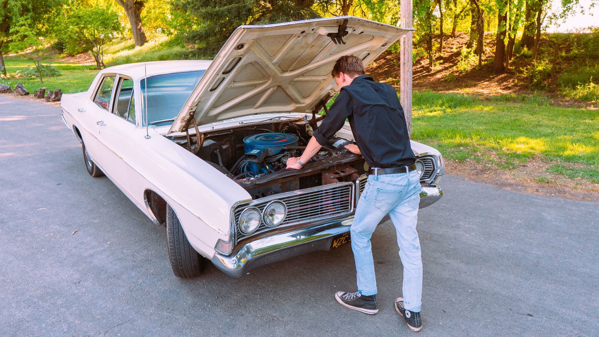 A man fixing a vintage car engine outdoors in Clarksburg, California, on a sunny day.