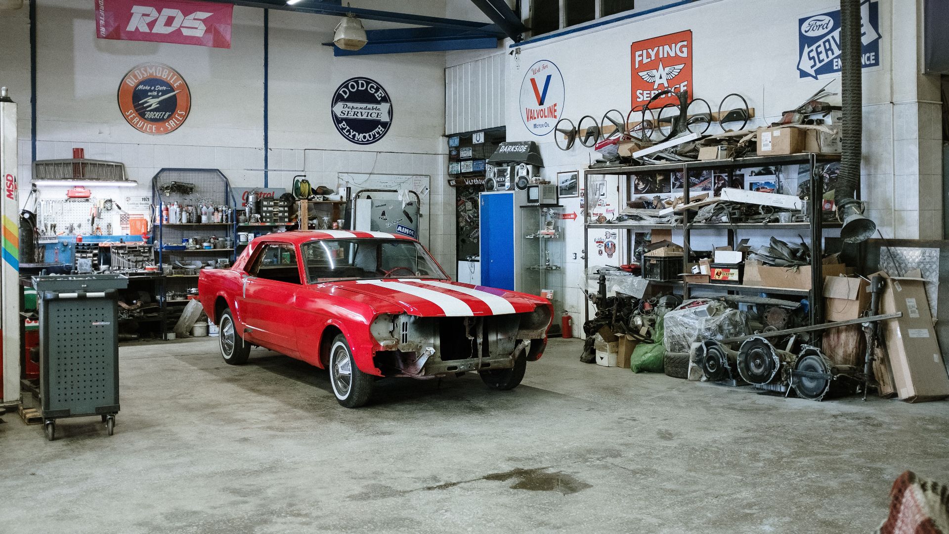 A vintage red car undergoing restoration in a well-equipped workshop with various tools and auto parts.