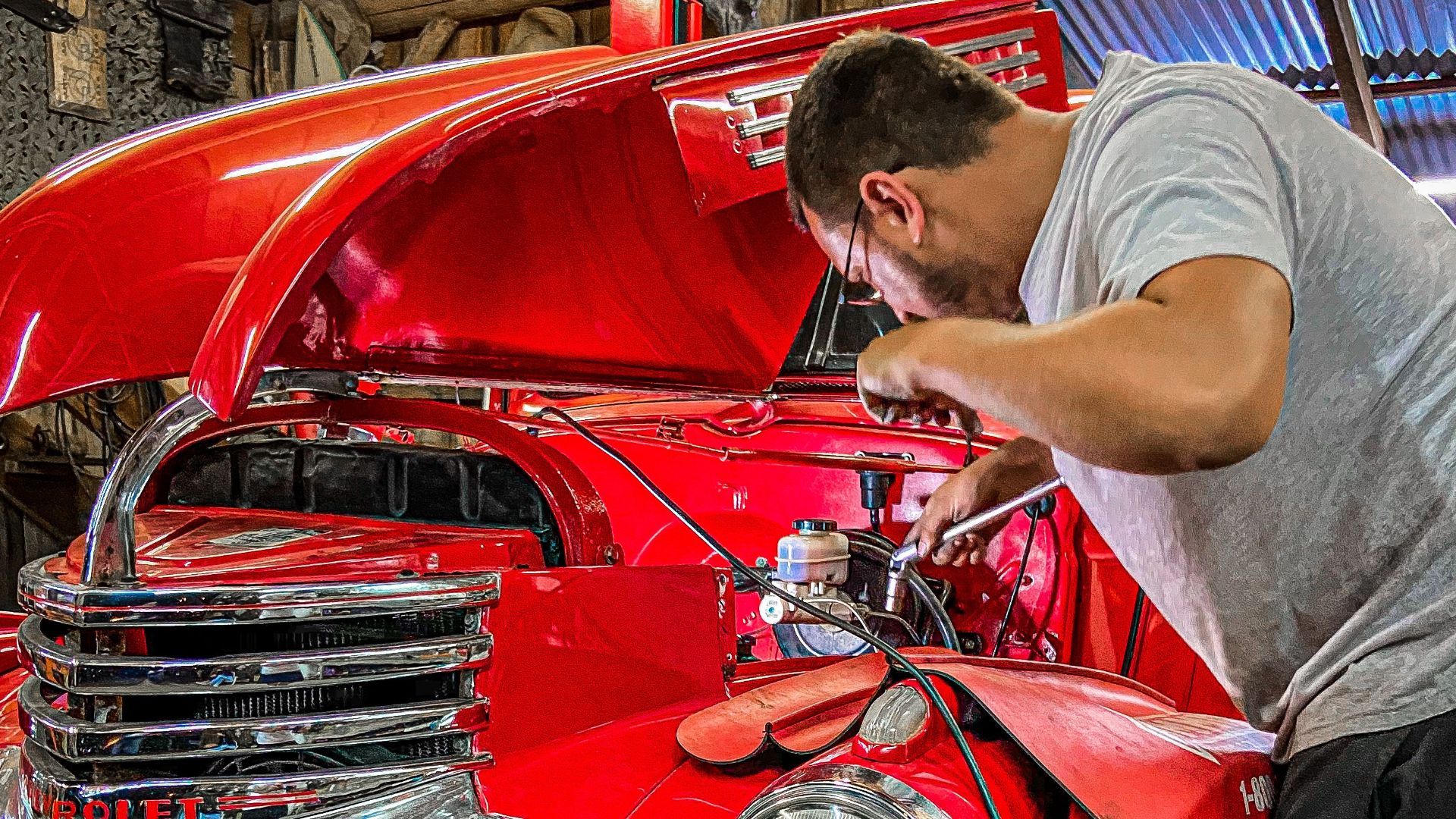 Man working on a vintage red car engine in an indoor workshop setting.