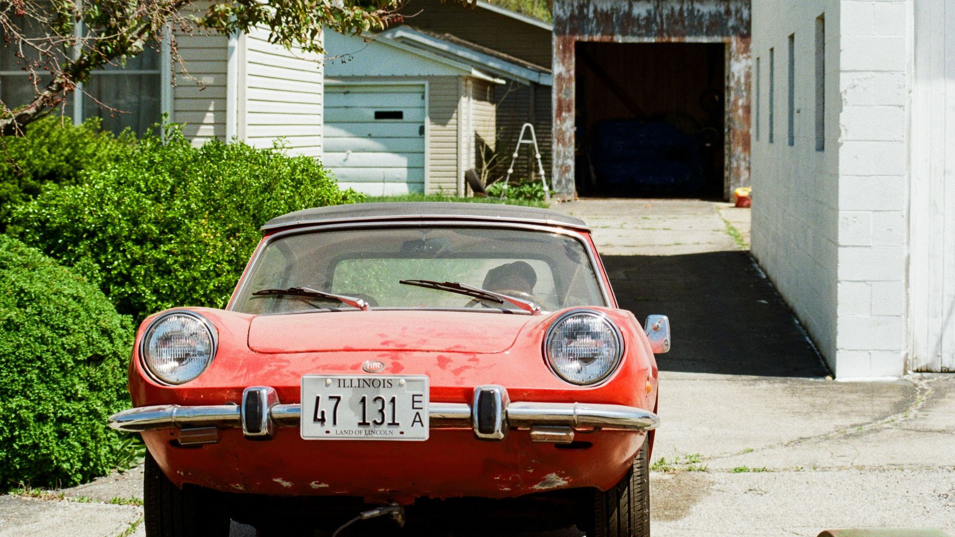 Red vintage sports car parked in a suburban driveway in Heyworth, Illinois, during spring.