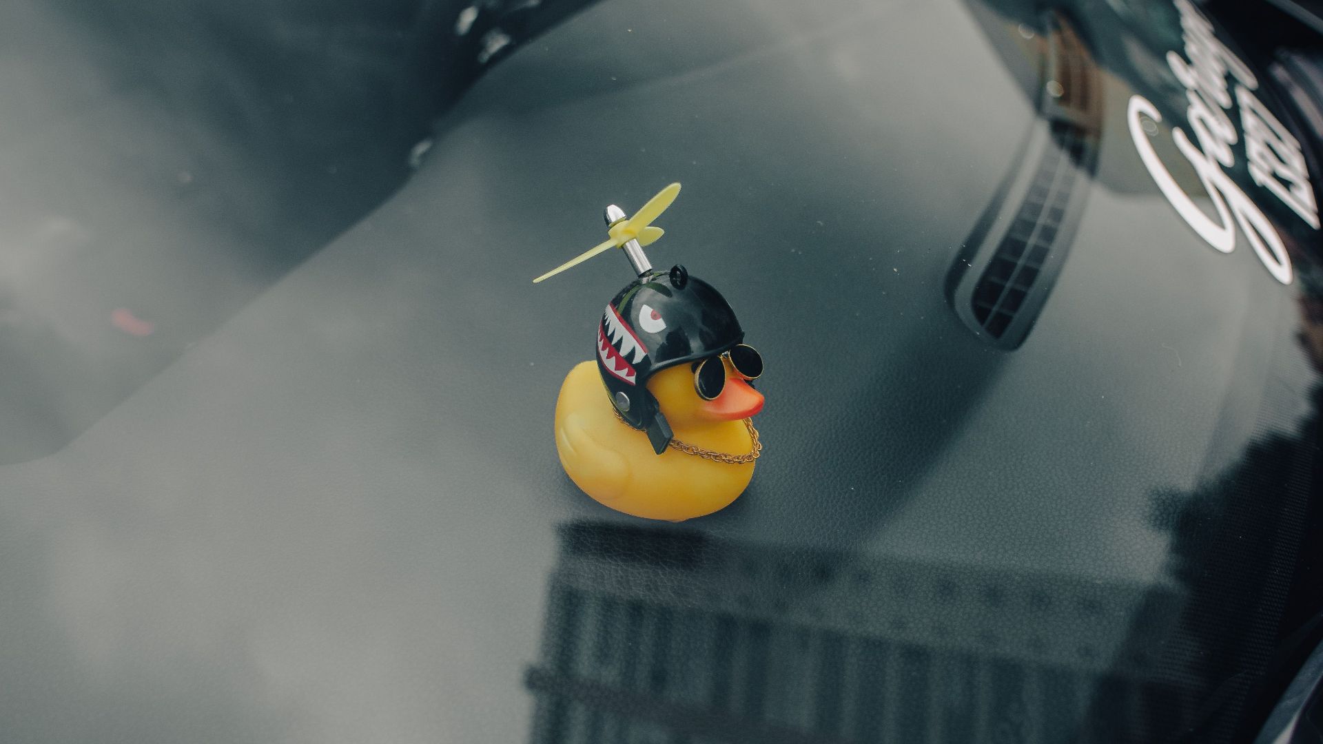 A quirky yellow rubber duck with a propeller and sunglasses placed on a car dashboard, reflecting the cityscape.