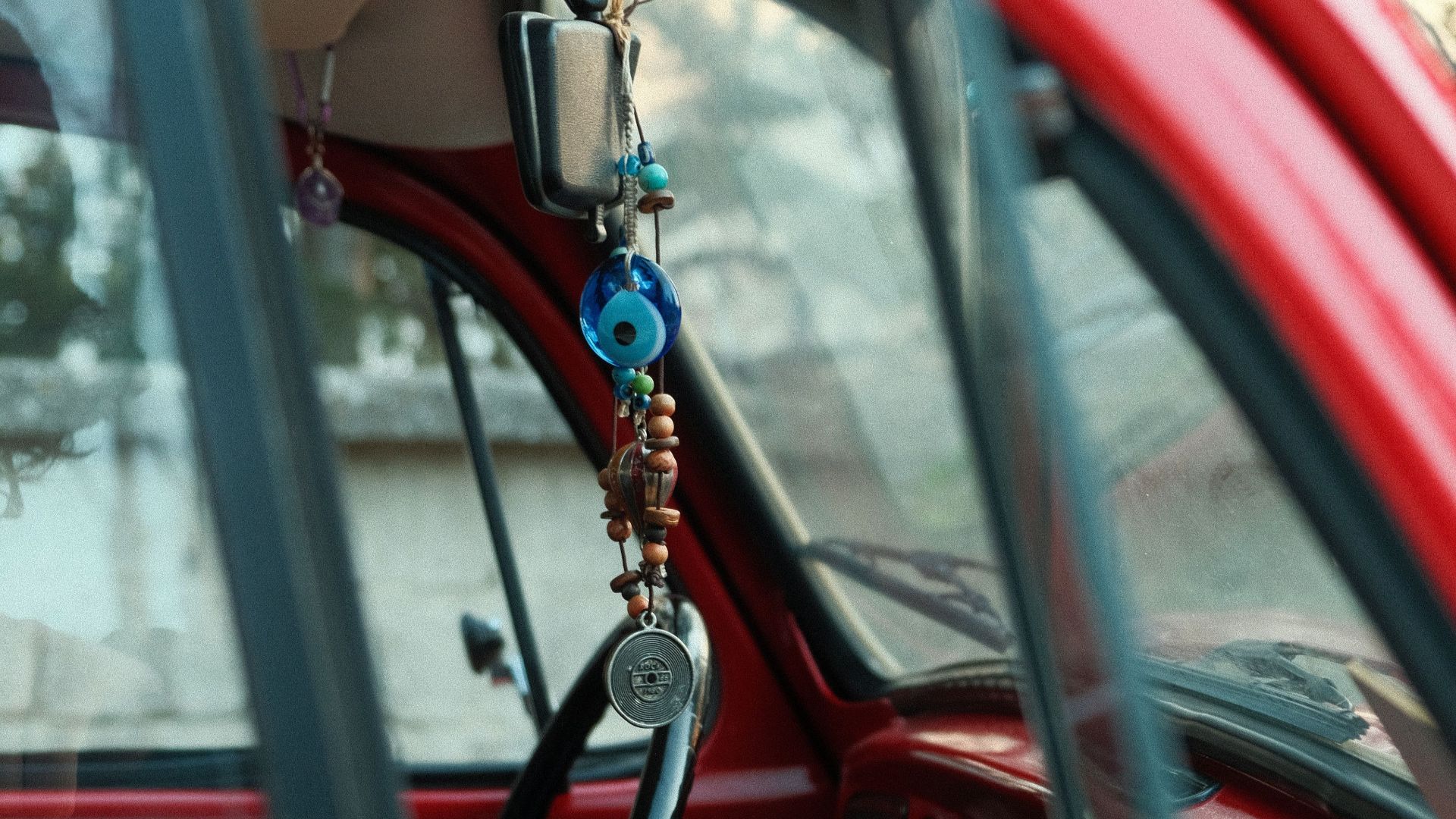 Detailed shot of a vintage red car's interior featuring hanging beads and a classic steering wheel.