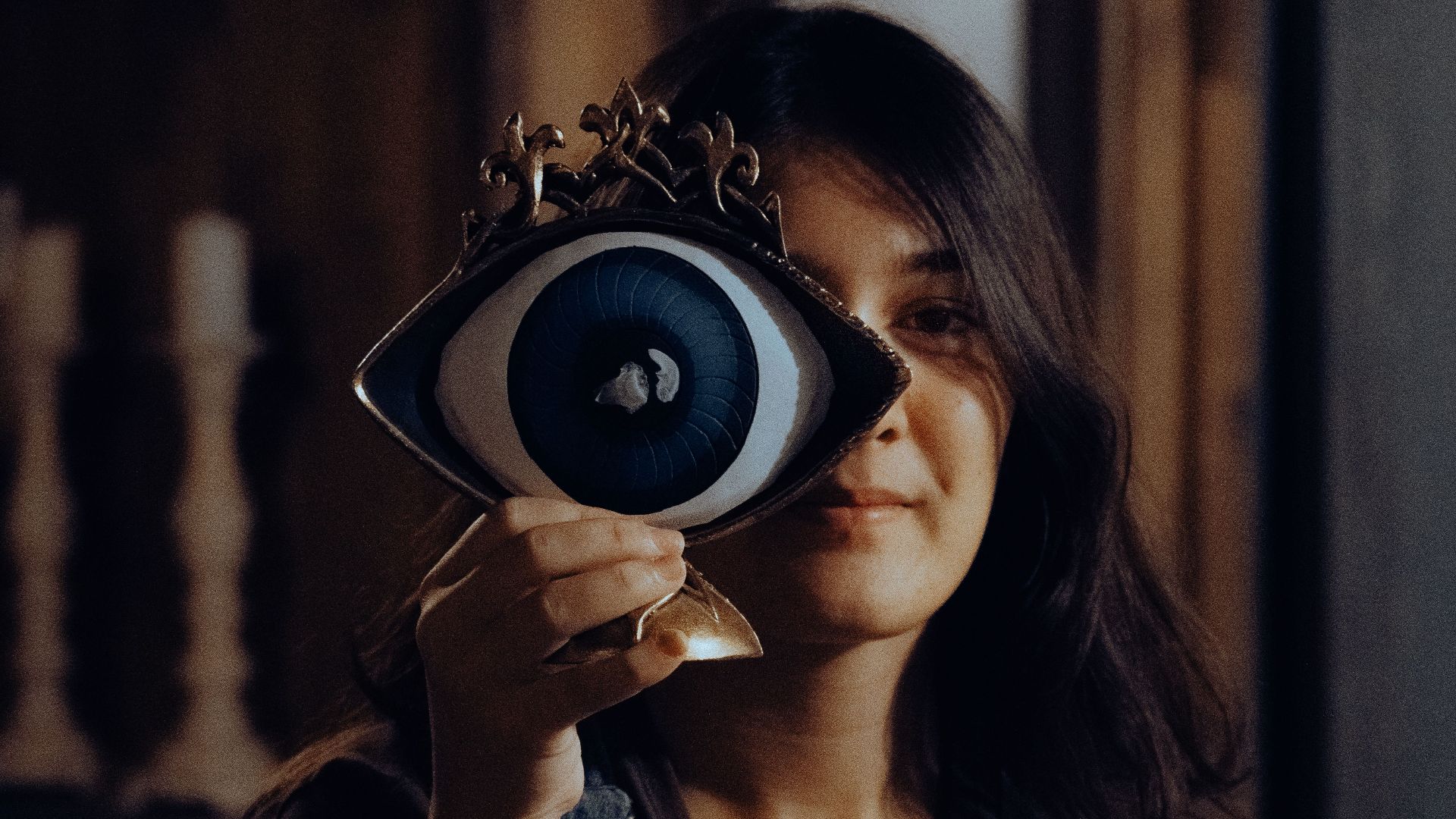 Young woman holding an artistic eye figurine, indoors with moody lighting.