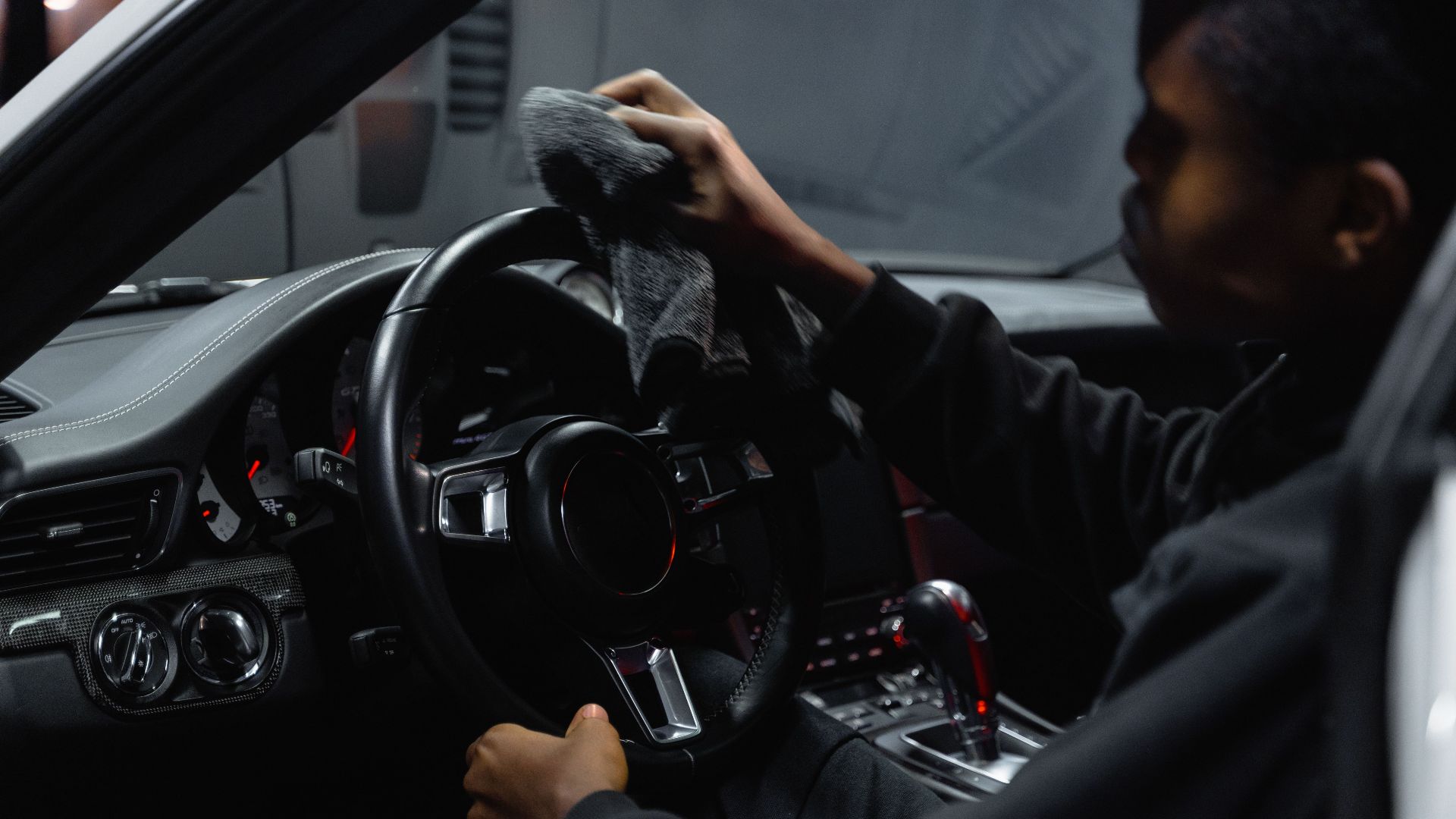 Adult man wiping a car steering wheel with a cloth inside a vehicle.