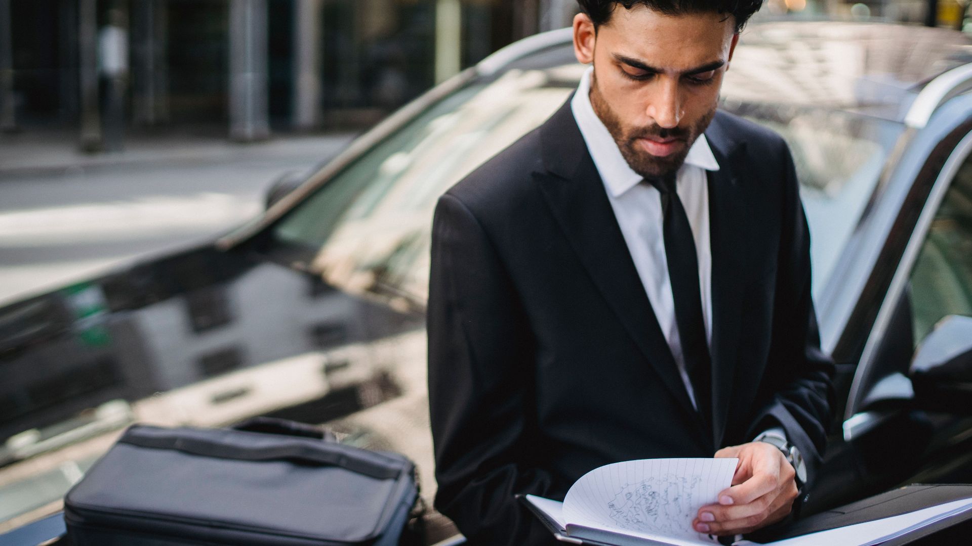 Confident businessman reviewing documents on the street beside a car.