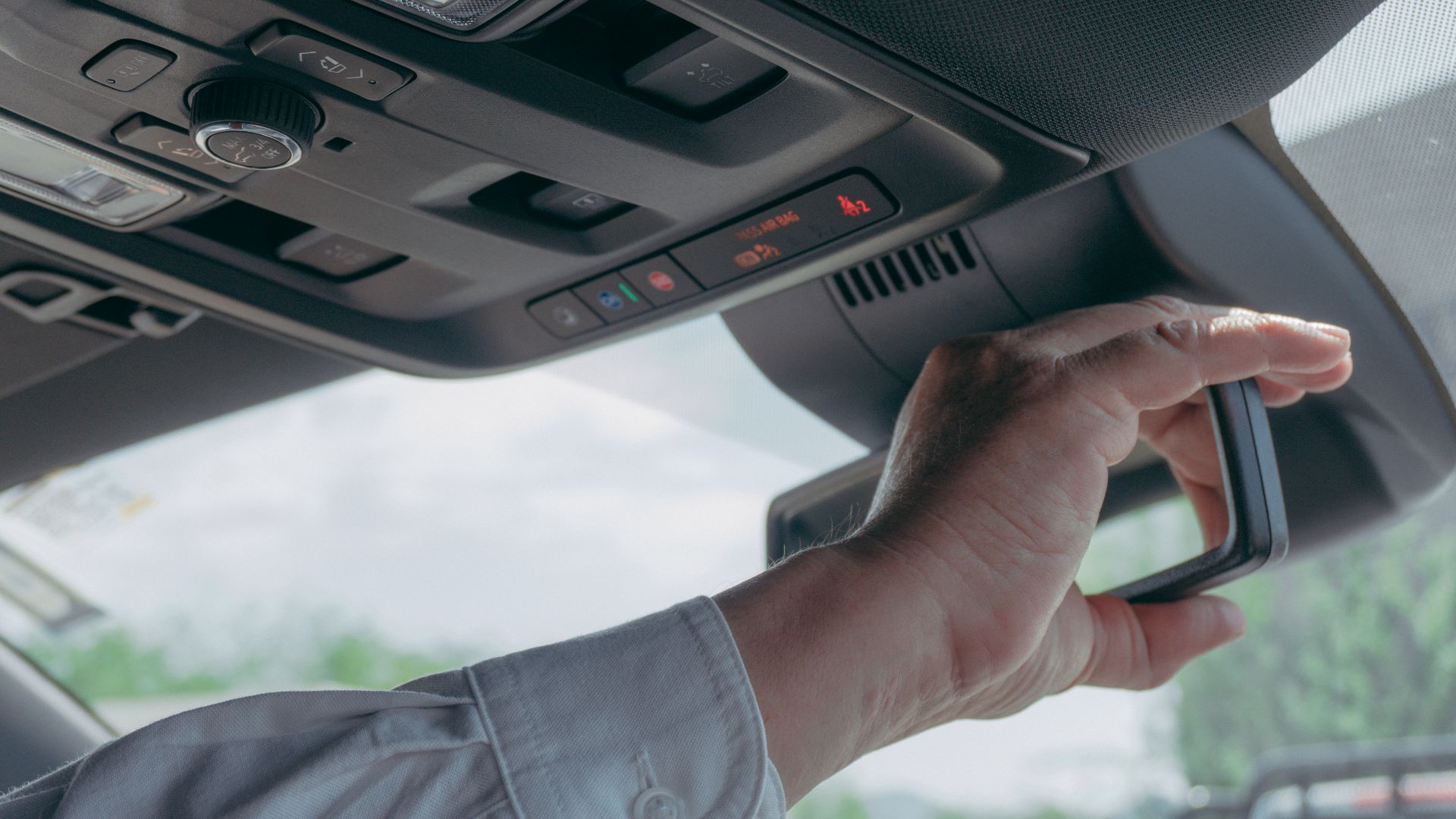 Close-up of a driver adjusting the rearview mirror inside a car, showcasing modern vehicle technology.