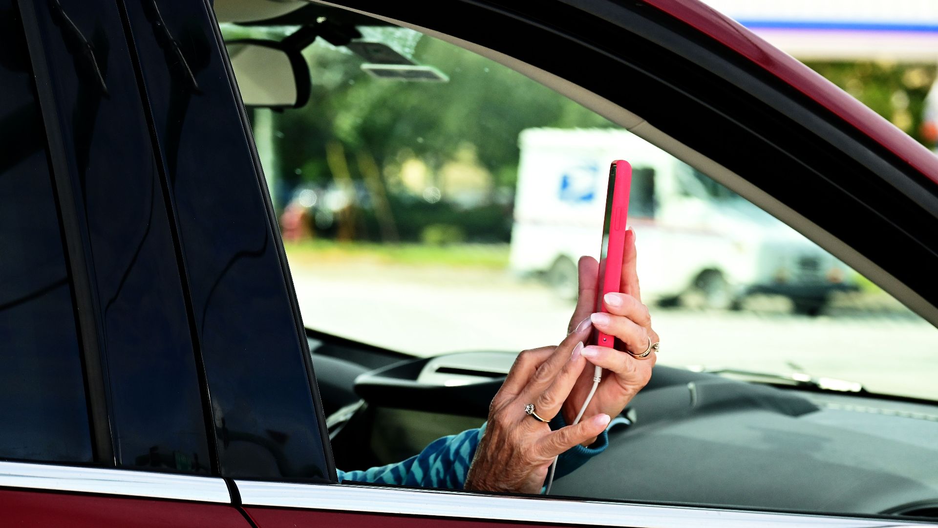 Senior woman taking pictures with smartphone from a car window, focusing on outdoor scene.