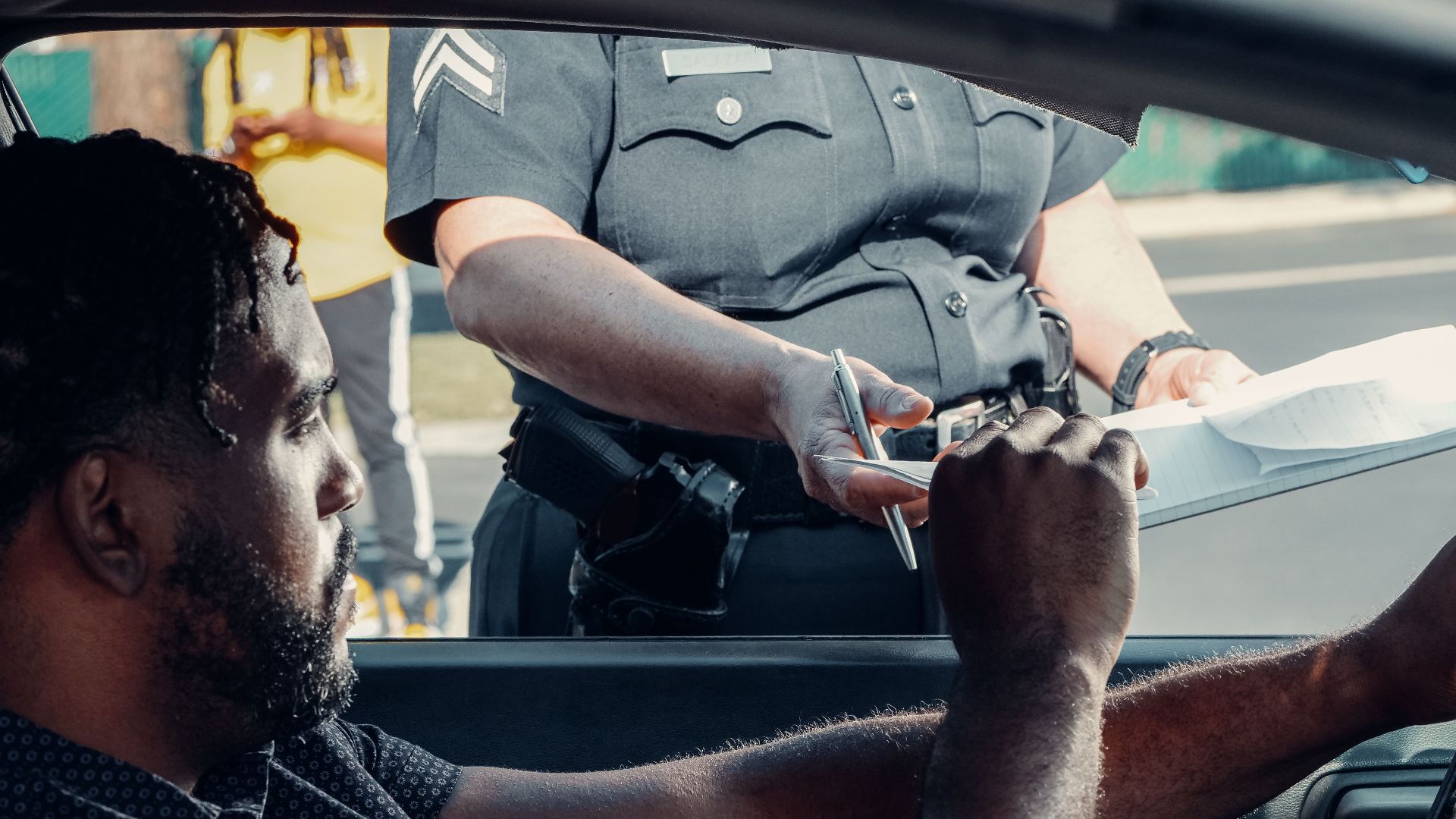 Police officer handing a traffic ticket to a driver during roadside inspection.