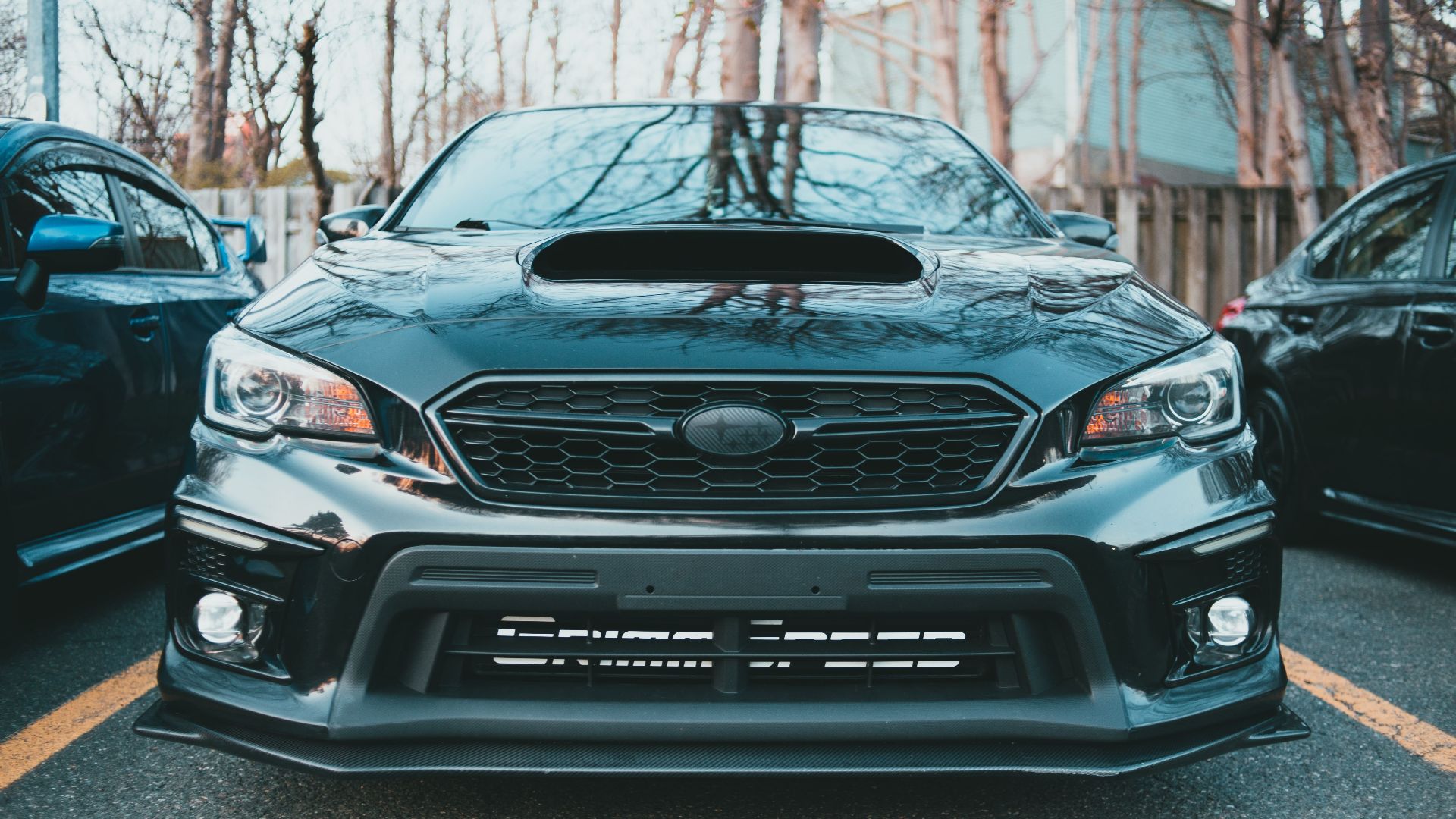 A sleek black Subaru Impreza with a prominent hood scoop, captured in an outdoor setting.