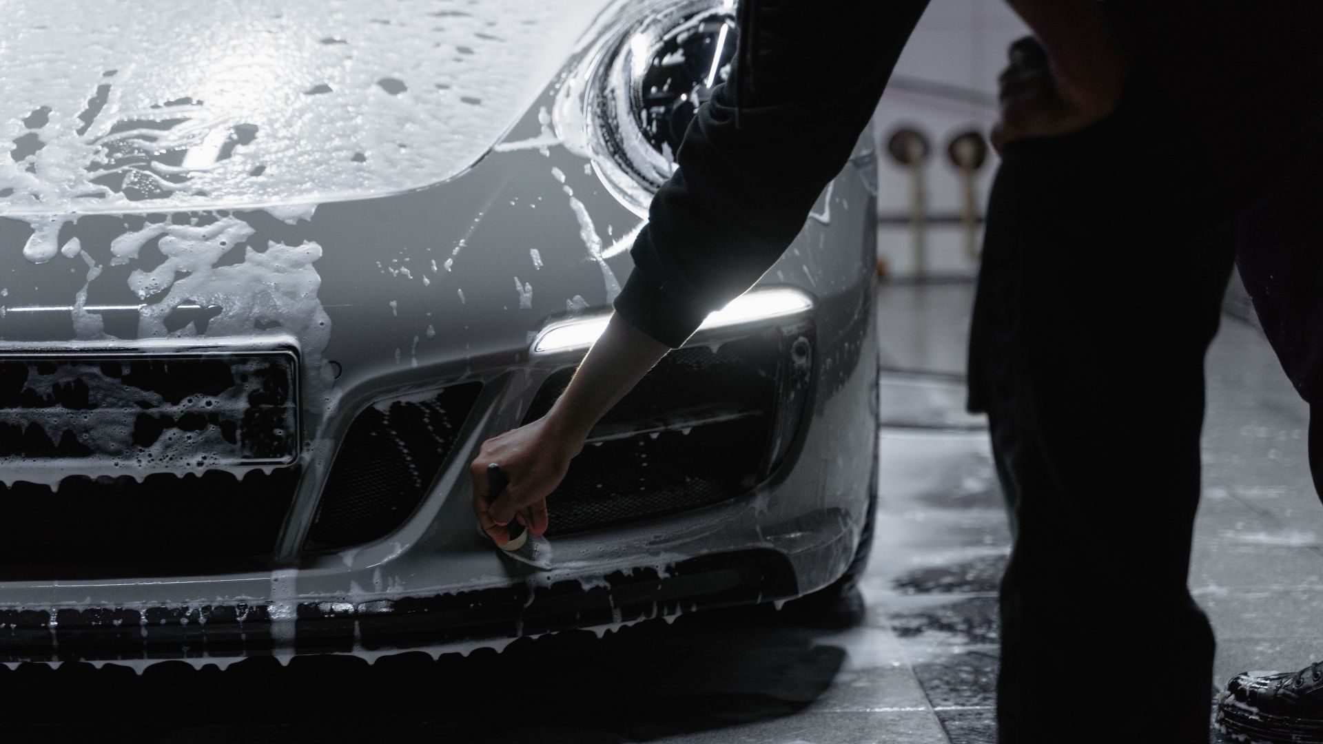 A close-up view of a car being meticulously washed with soap in a garage setting, emphasizing cleanliness and care.