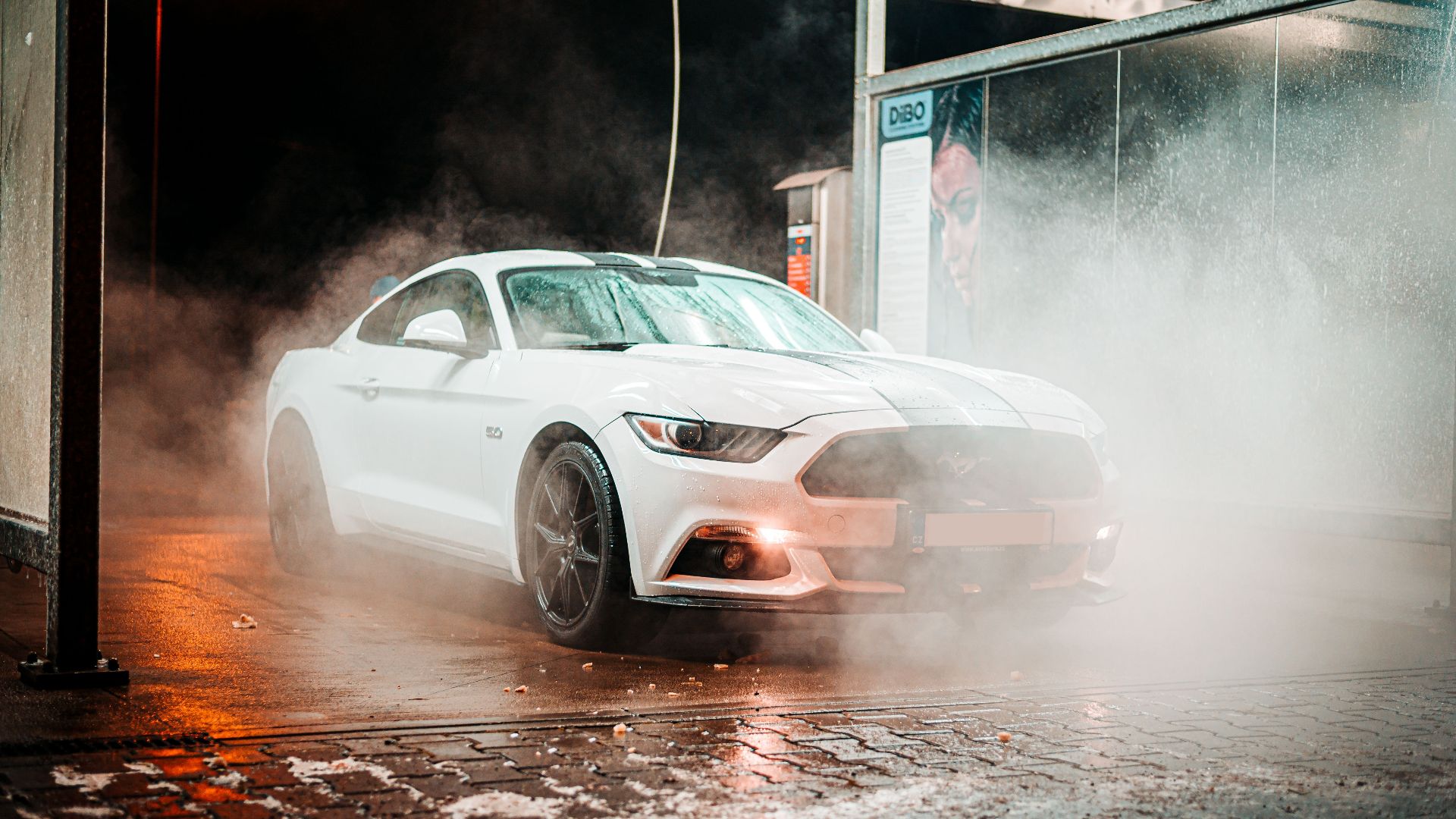 White Ford Mustang in a misty carwash setting, illuminated at night in an urban environment.