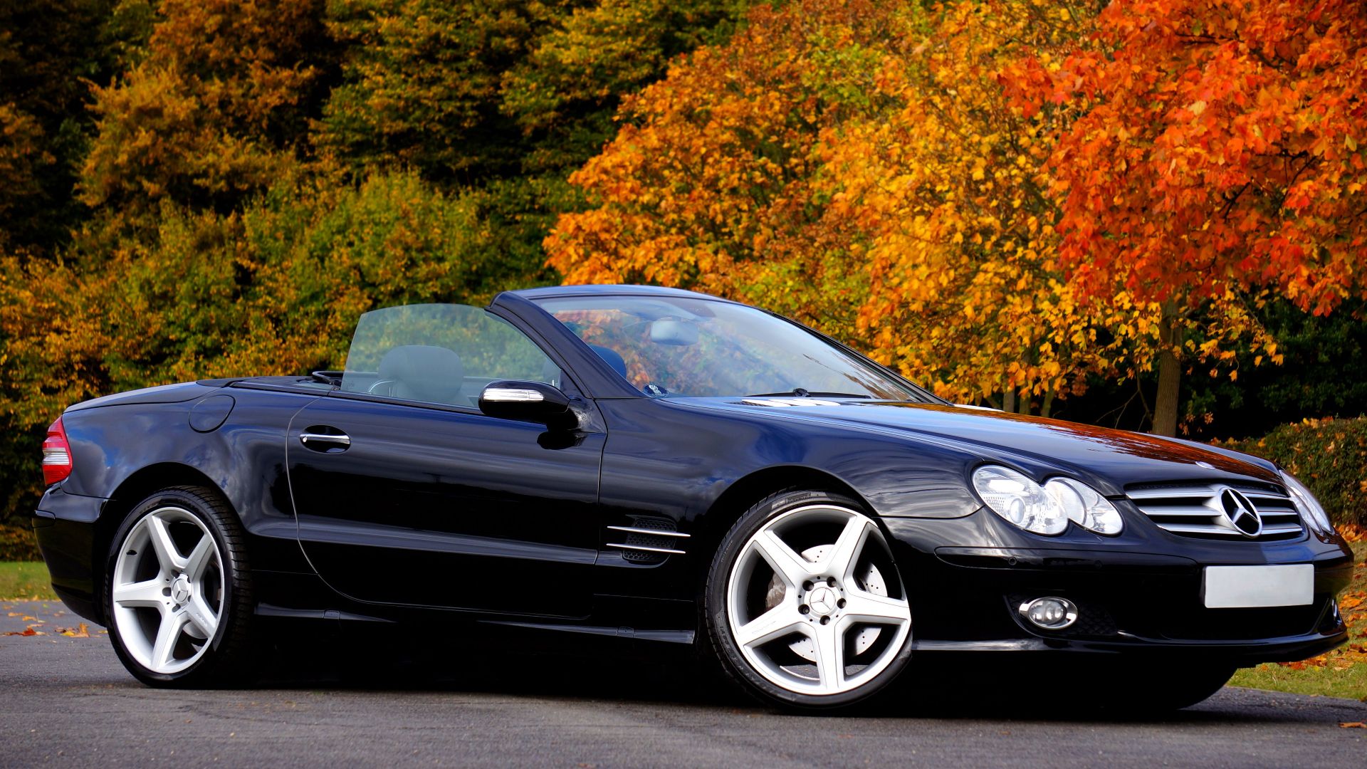 Black convertible car parked outdoors surrounded by fall foliage. Perfect for luxury travel imagery.