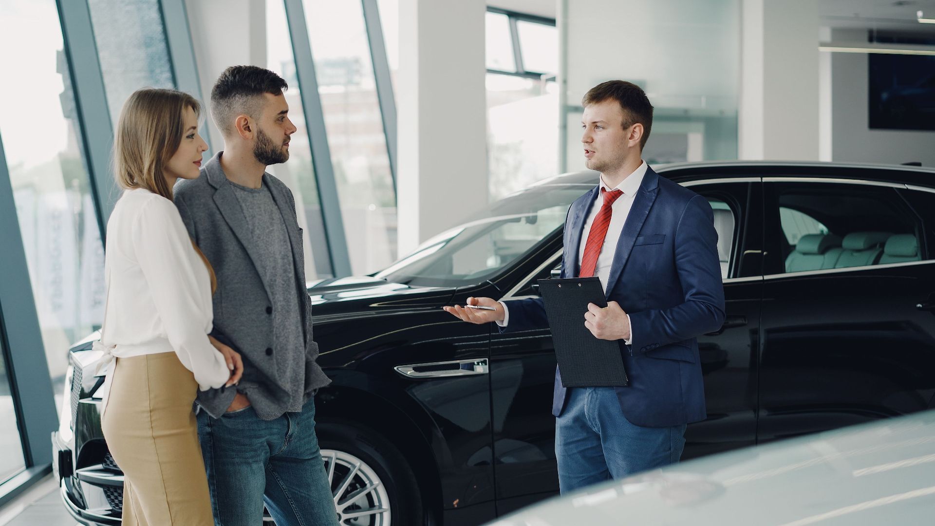 A couple talks with a salesman in a modern car showroom, considering a vehicle purchase.