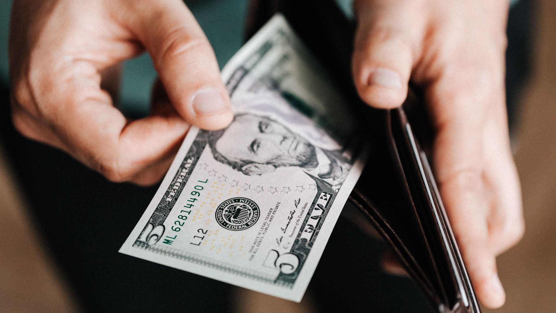Closeup of crop male in casual clothes taking dollars out of wallet while paying in shop