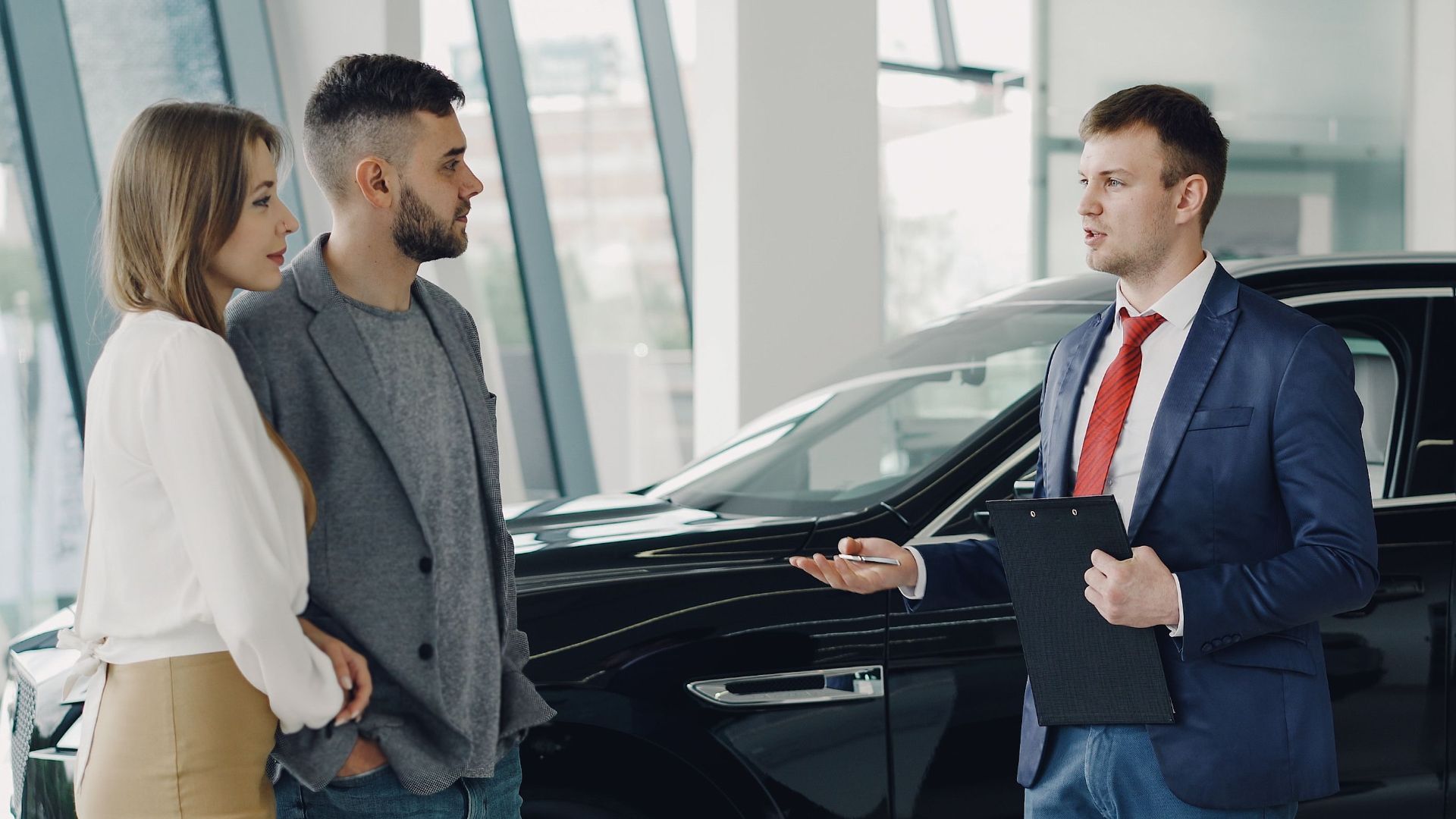 A couple talks with a salesman in a modern car showroom, considering a vehicle purchase.
