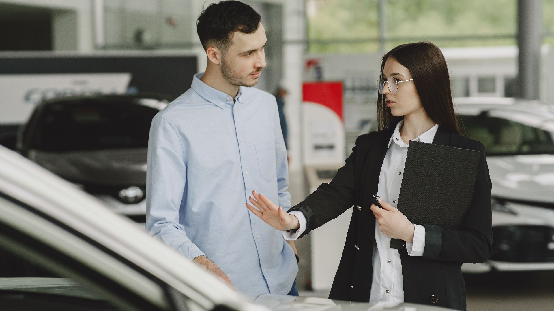 A salesperson and customer discussing car features in a dealership setting.