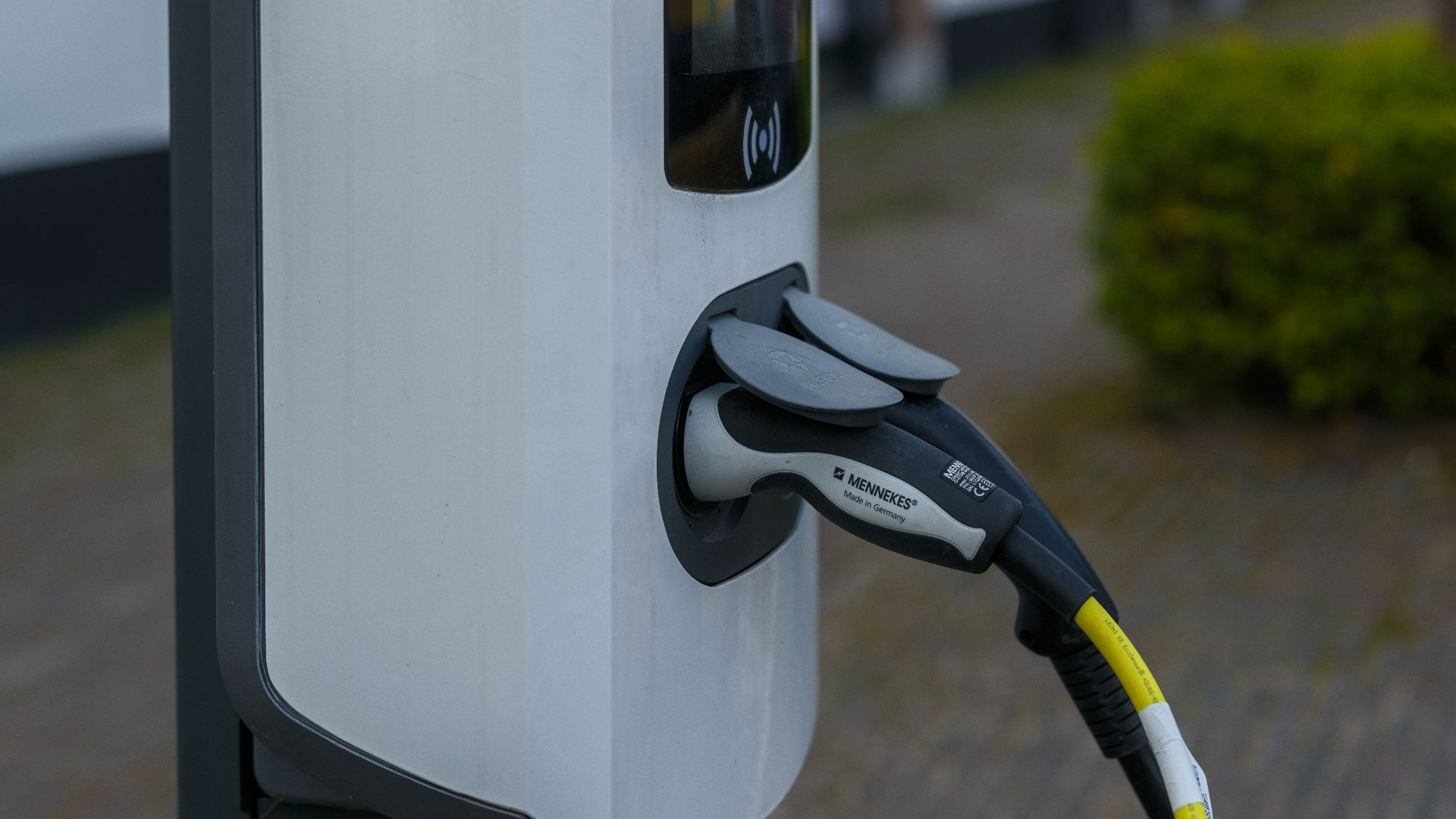 Close-up of an electric vehicle charging station with cable and plug outdoors.
