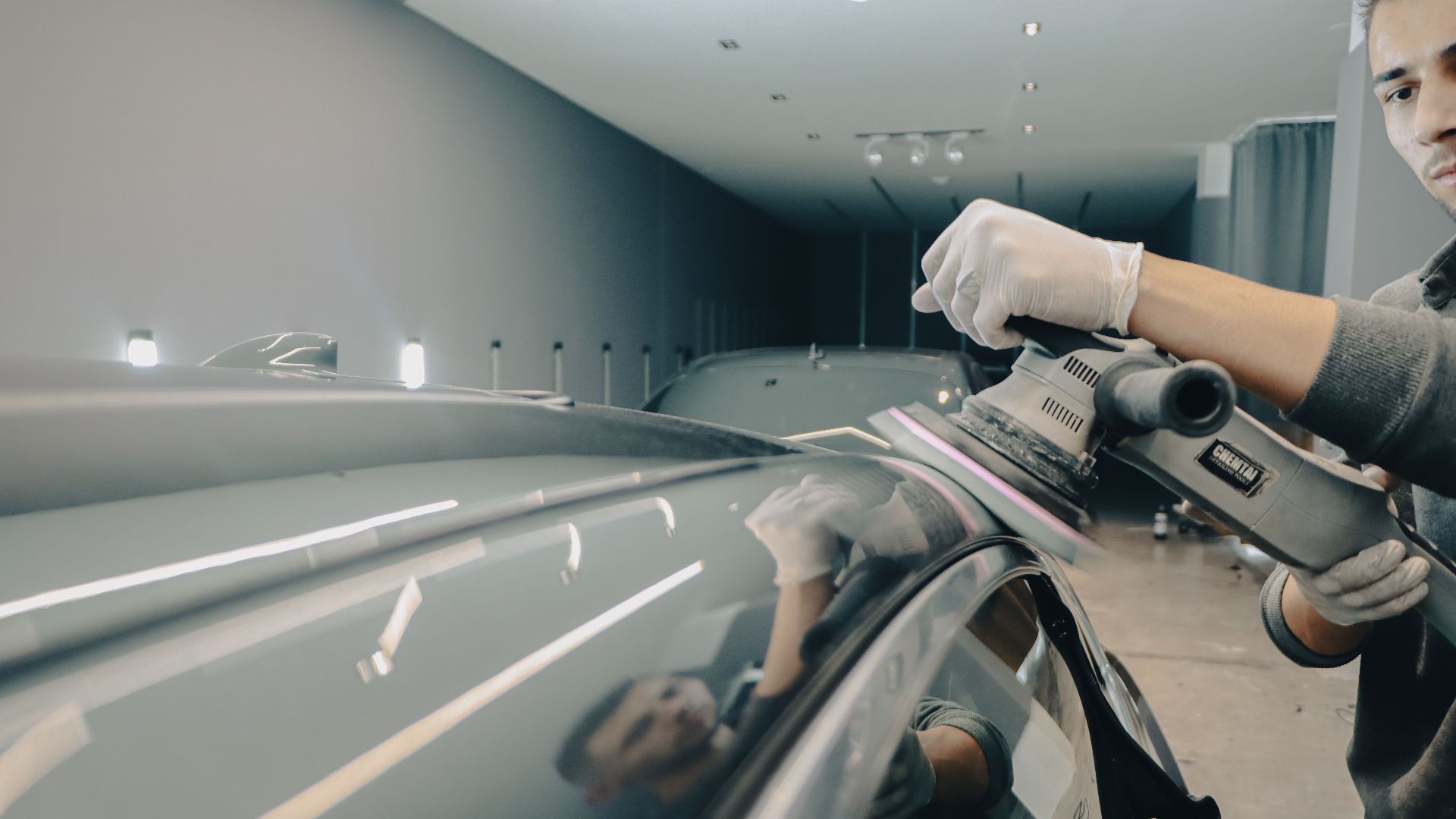 Worker using electric polisher on car roof for a shiny finish in an auto workshop.