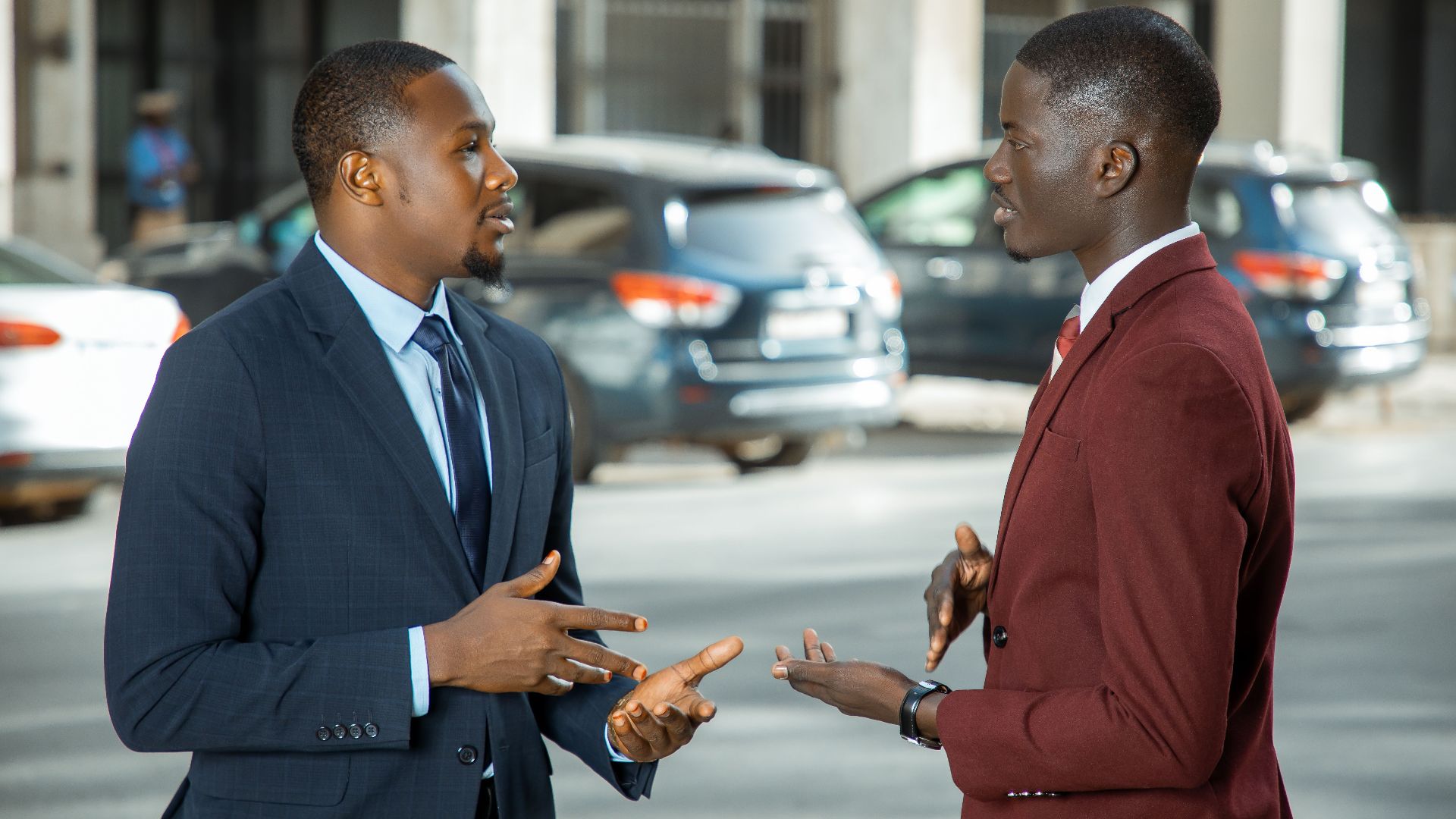 Two African businessmen in formal suits have a discussion on a city street in Dakar, Senegal.