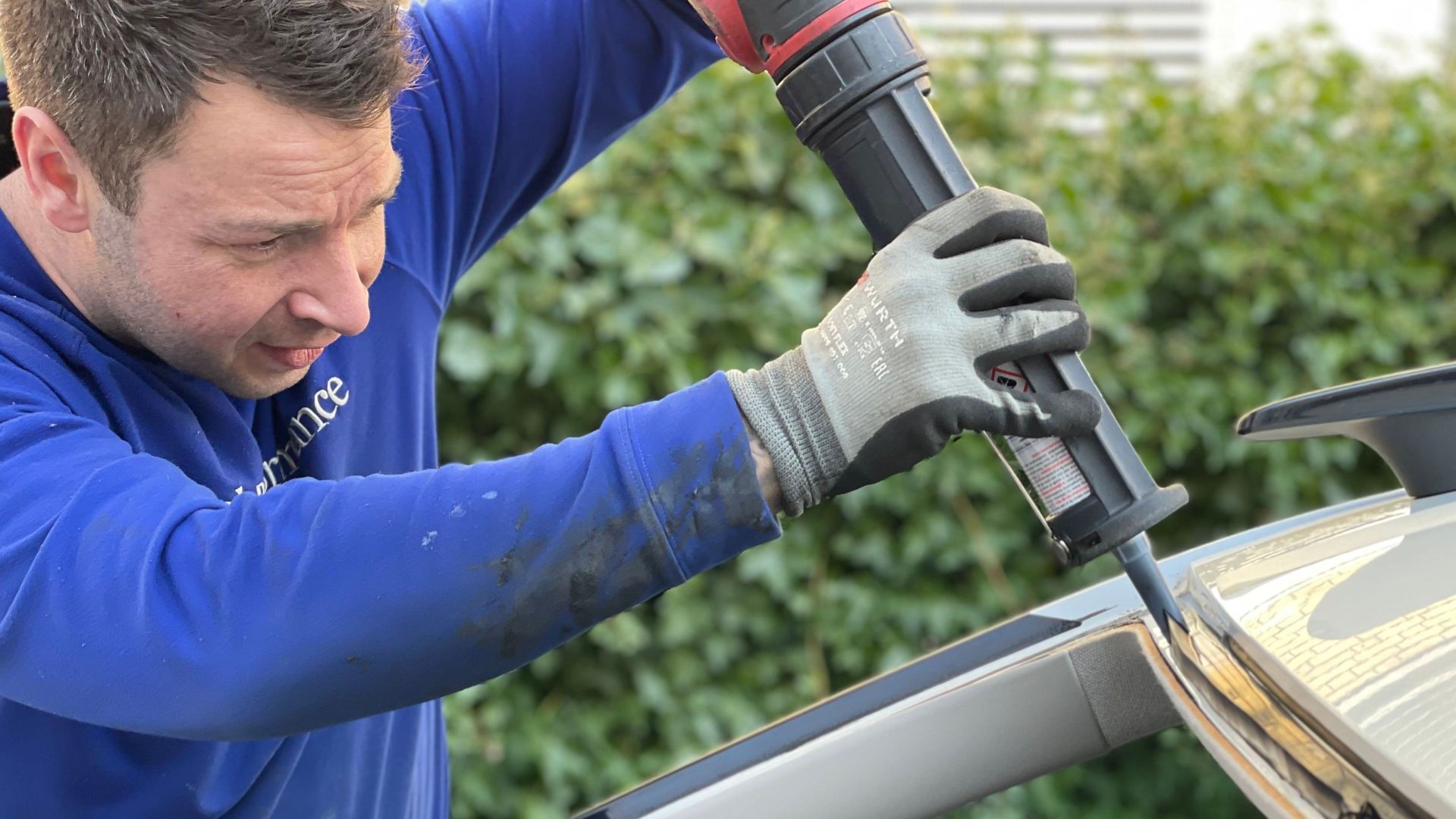 Man carefully applies glue to repair car windshield in Copenhagen outdoor setting.