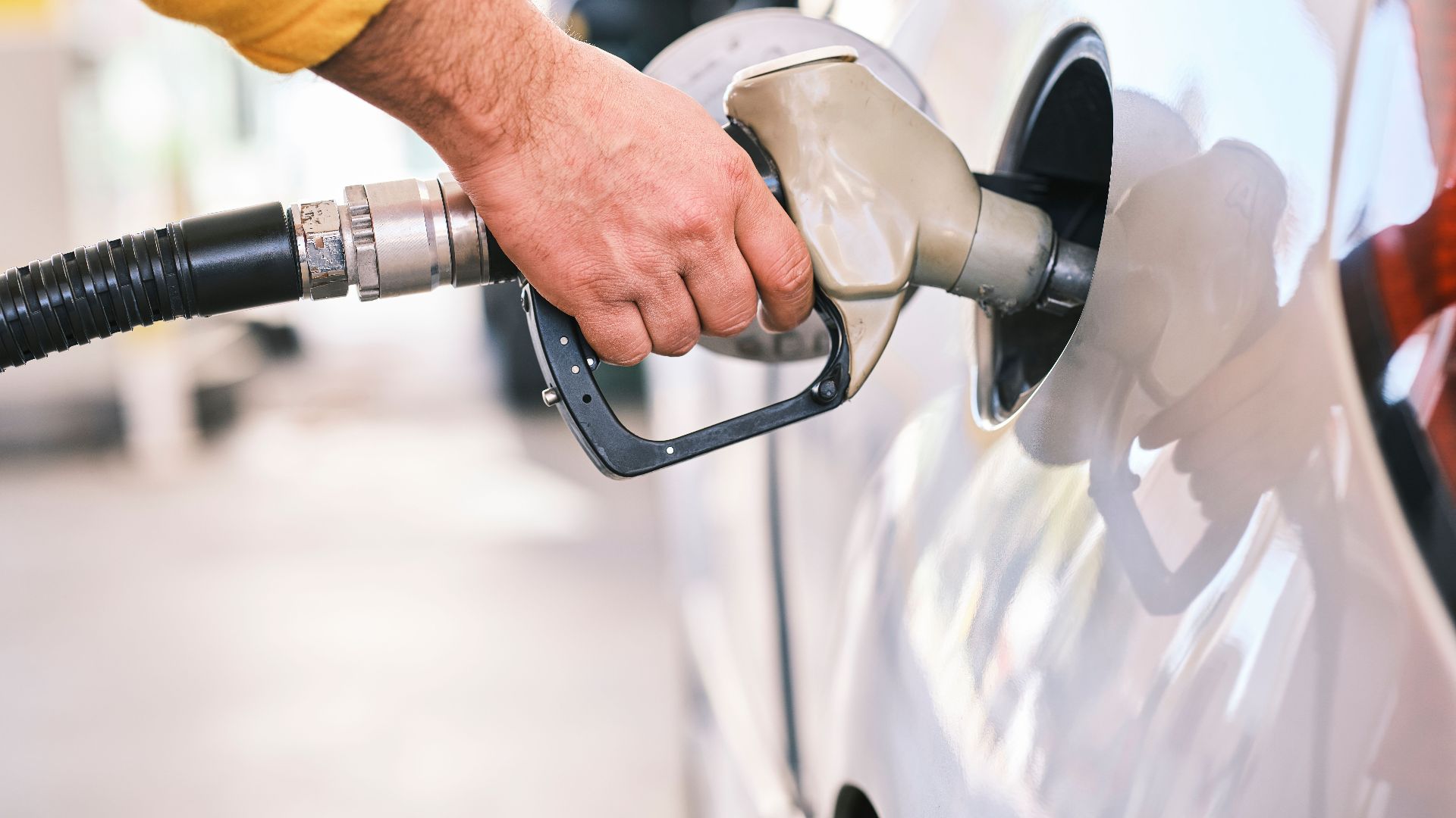 Close-up of a person refueling a car with a gas nozzle at a station.