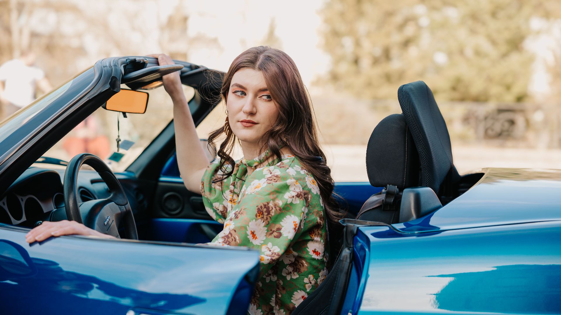 Stylish woman enjoying a drive in a blue convertible on a sunny day.