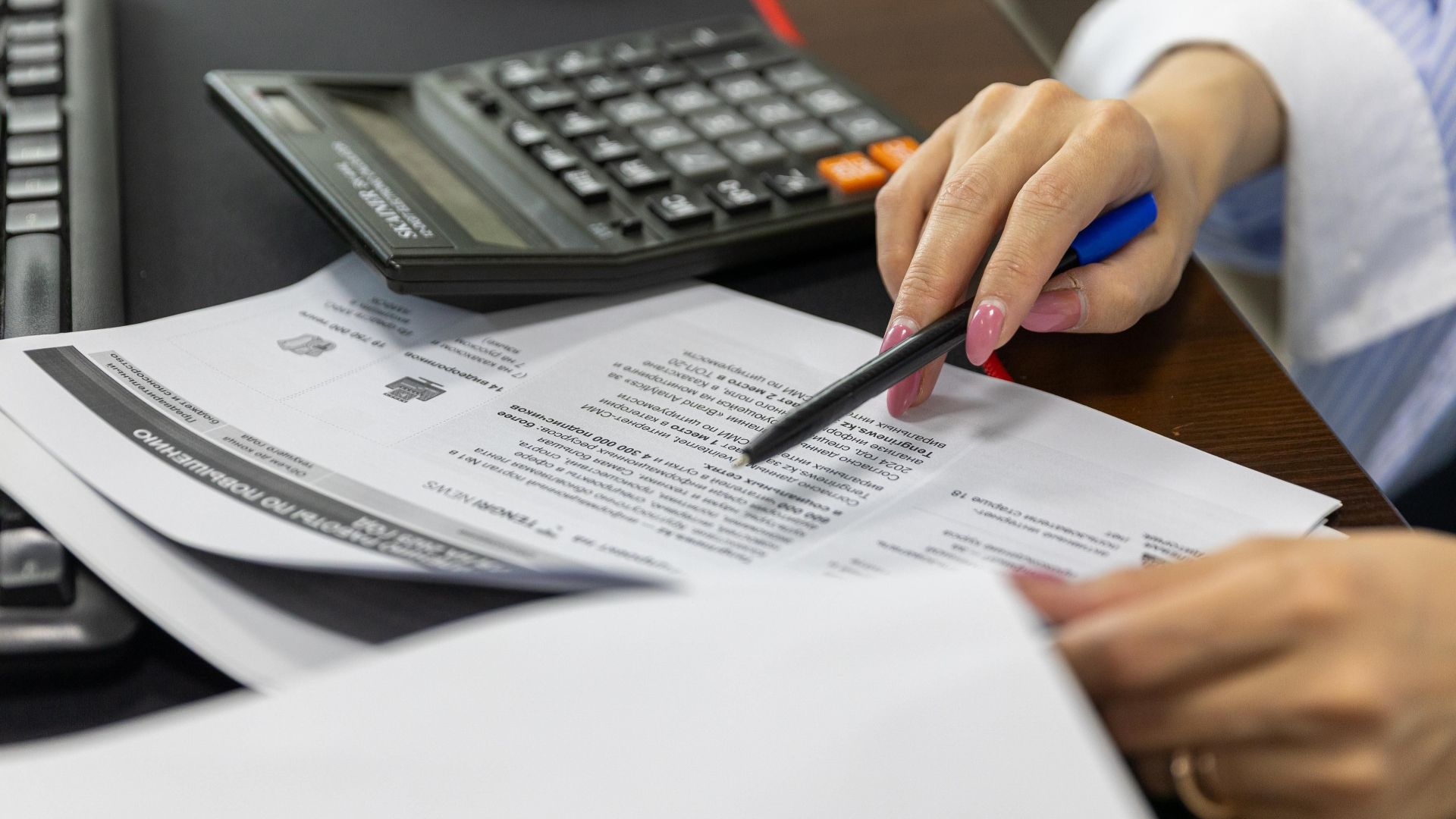 Close-up of a woman's hand reviewing financial documents with a calculator.