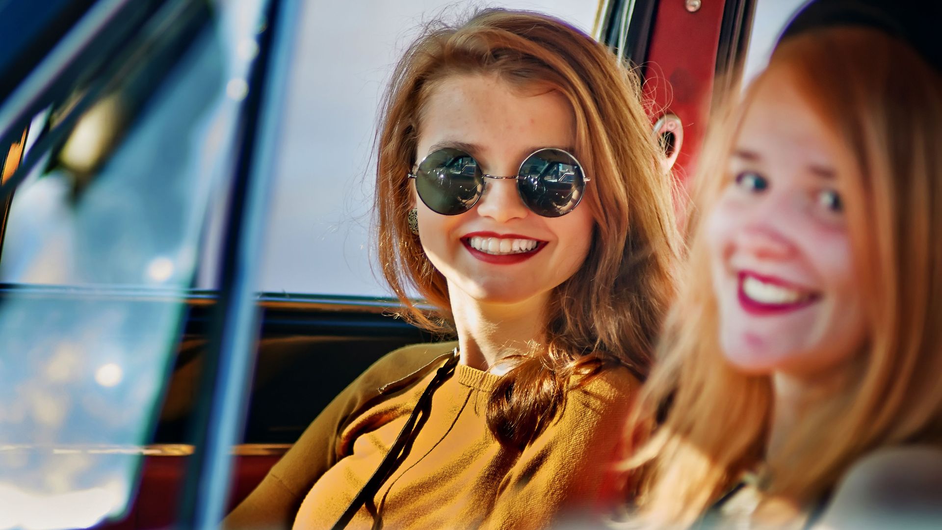 Two smiling young women in sunglasses enjoying a car ride on a sunny day.