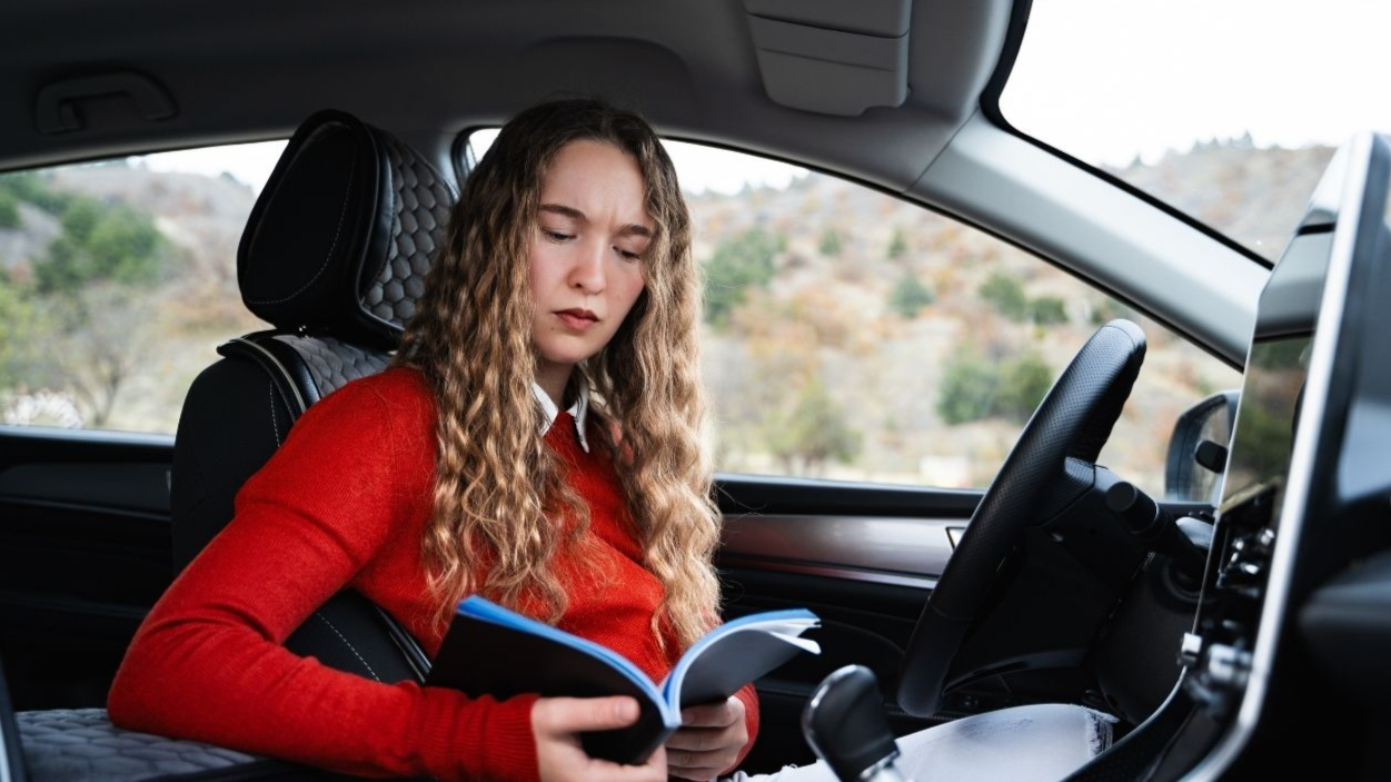 Shutterstock-2574928741, A young puzzled woman reads the car manual because of a problem with the new car. A worried female driver in casual wear reading the owner's manual of her auto. Buy or rent an automobile.