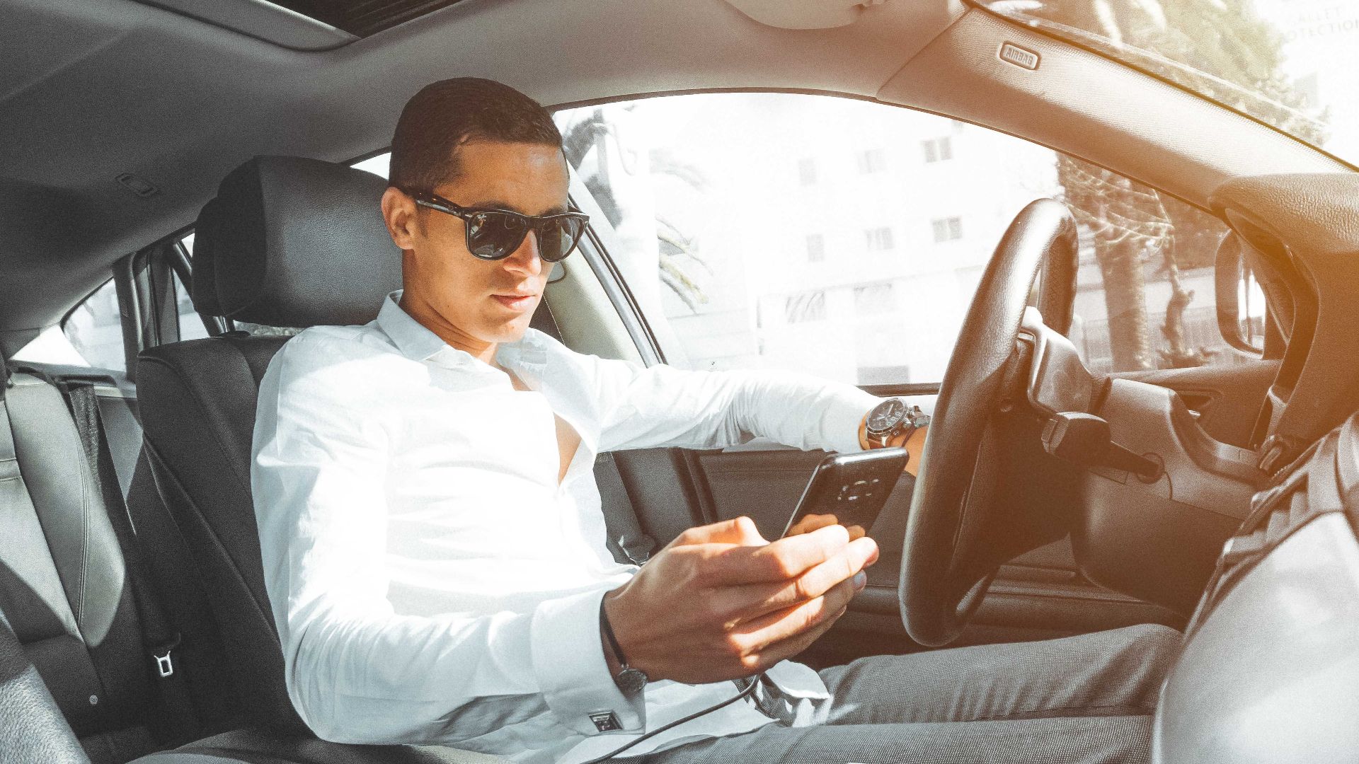A man wearing sunglasses texts on his phone while driving a car in Morocco.